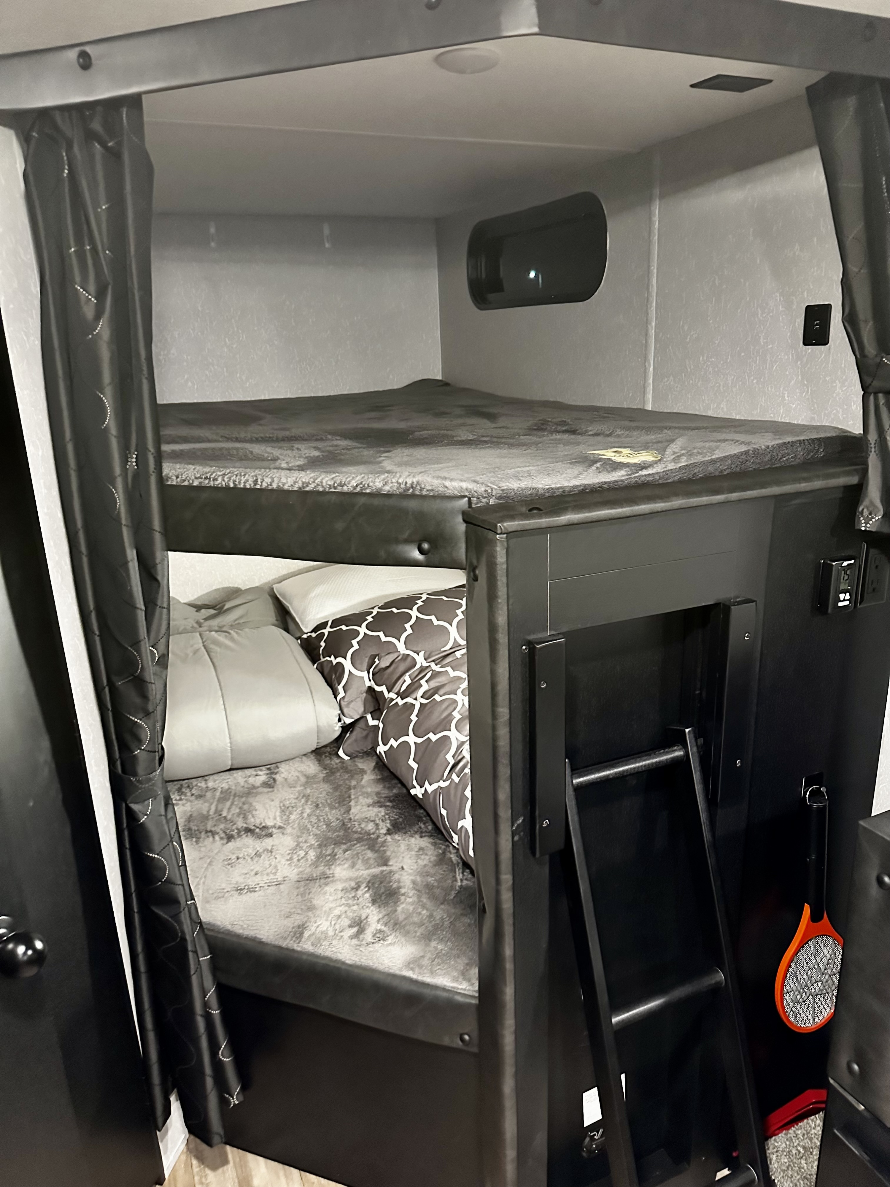 Cozy bunk beds inside an RV rental, complete with a ladder, privacy curtains, and grey bedding. Ideal compact sleeping area.. Forest River Cherokee Grey Wolf Black Label 2021