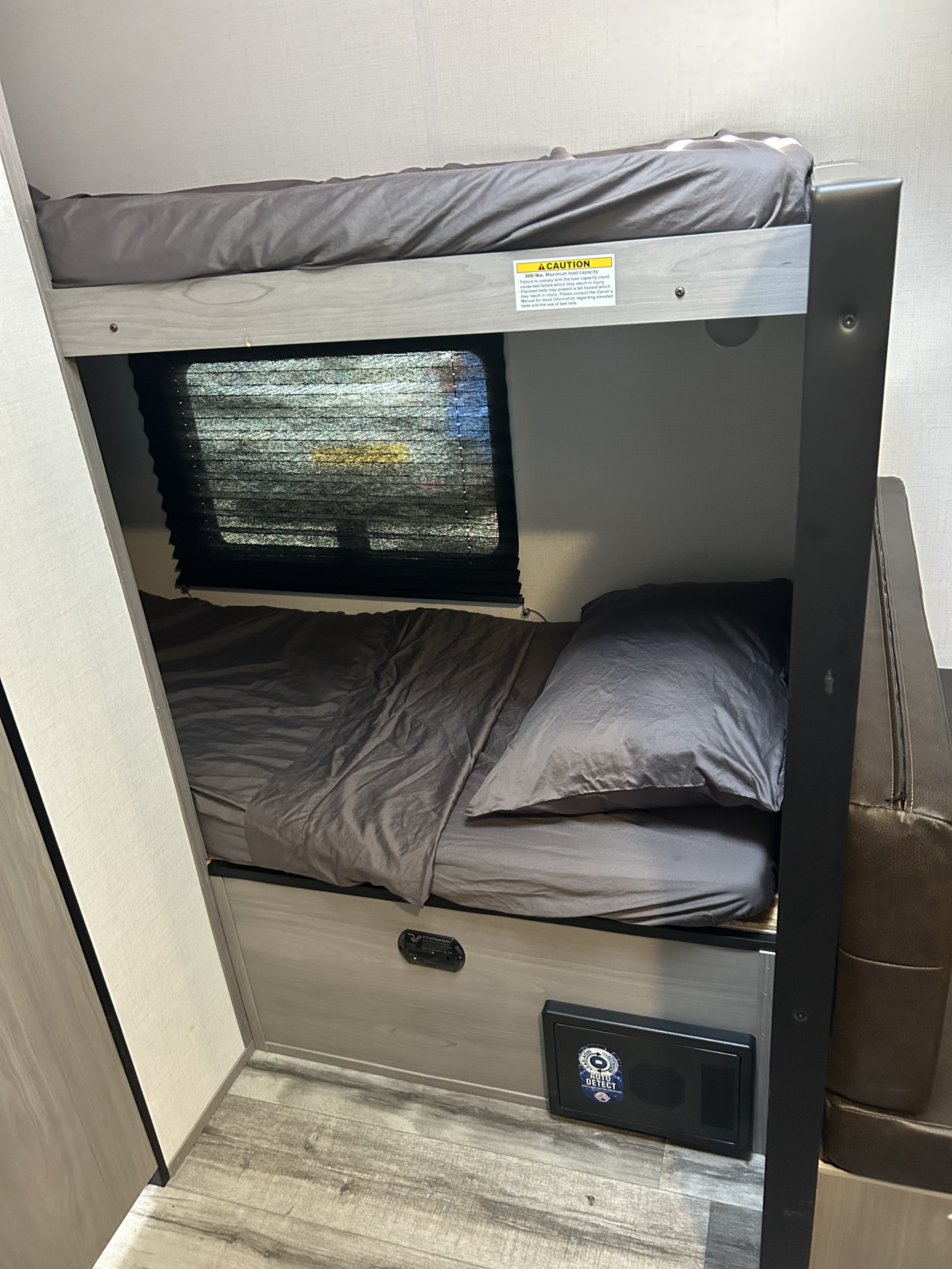 Compact bunk beds in an RV rental with gray bedding. Features a window, safety label, and detectors for safe travels.. Dutchmen Coleman Lantern LT 2023