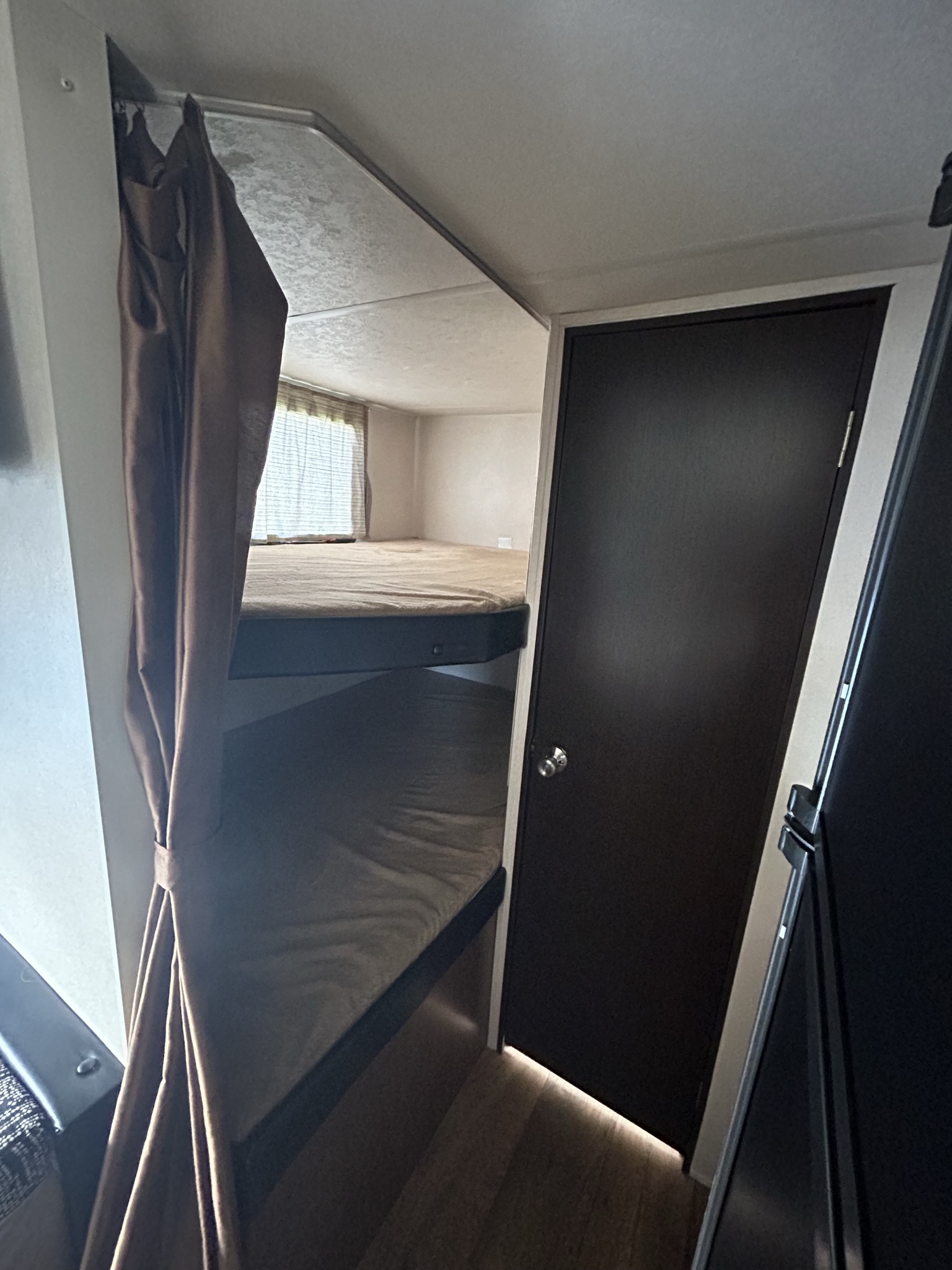 An RV rental's sleeping area, showing two bunk beds with a privacy curtain and a dark interior door.. Forest River Wildwood X-Lite 2017