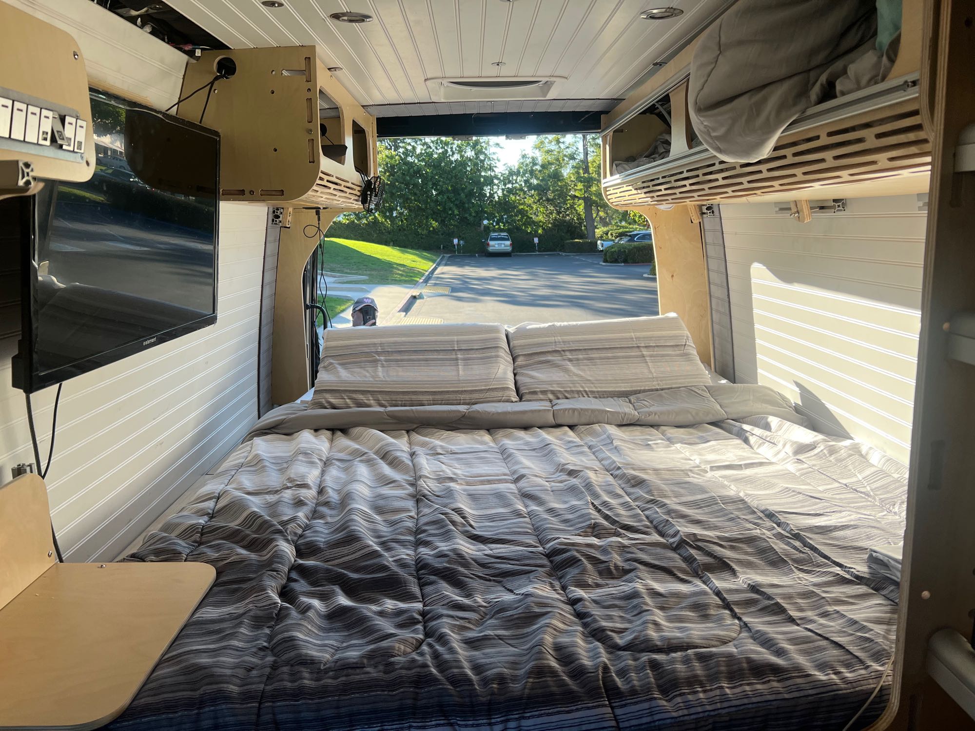This RV rental's custom interior features a comfy bed, mounted TV, and smart storage, opening to a peaceful parking lot.. Mercedez Sprinter 2014