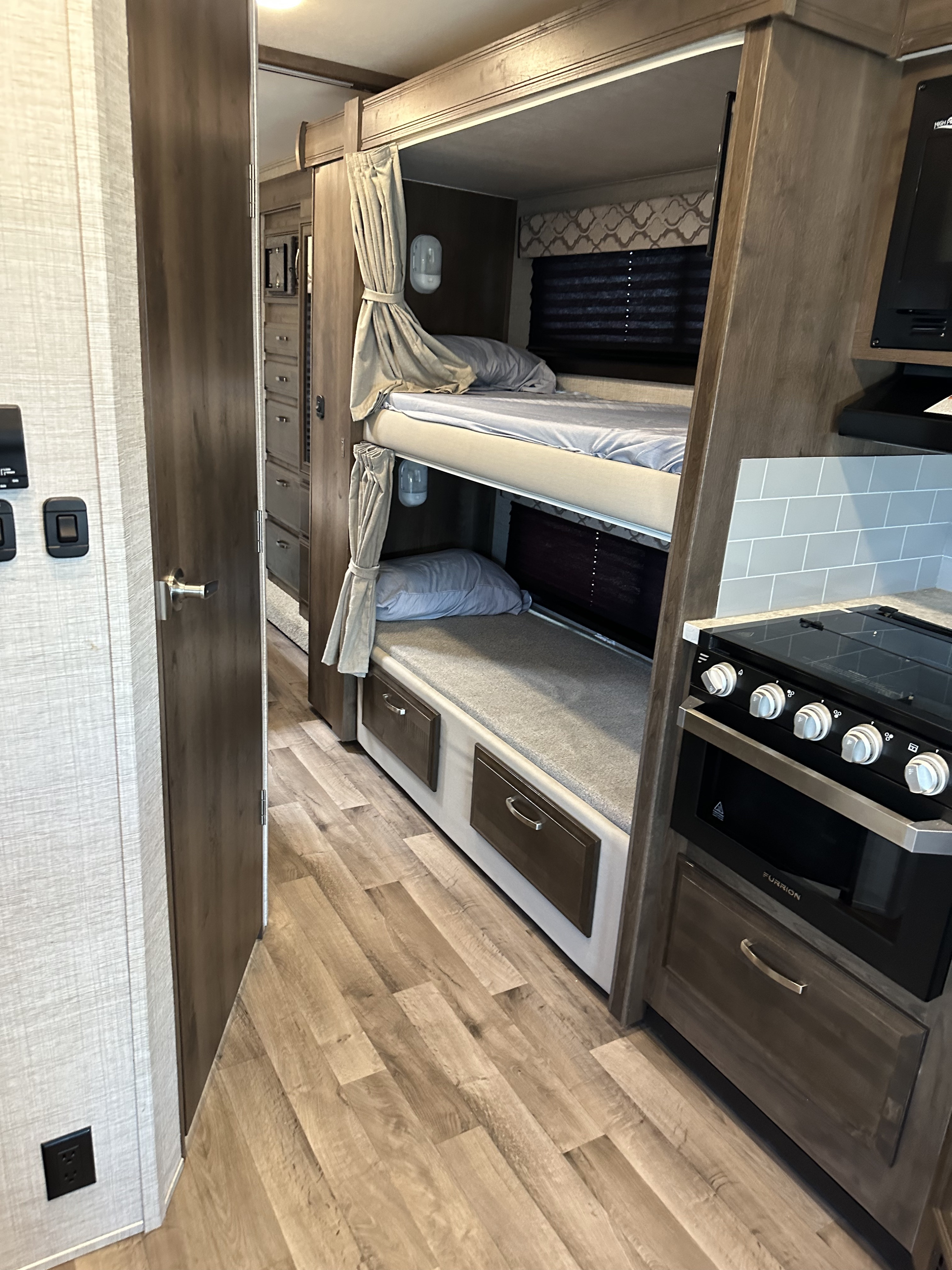 RV rental featuring two cozy bunk beds with light bedding, a compact kitchen with a stove, and wood-look flooring.. Jayco Redhawk 2021