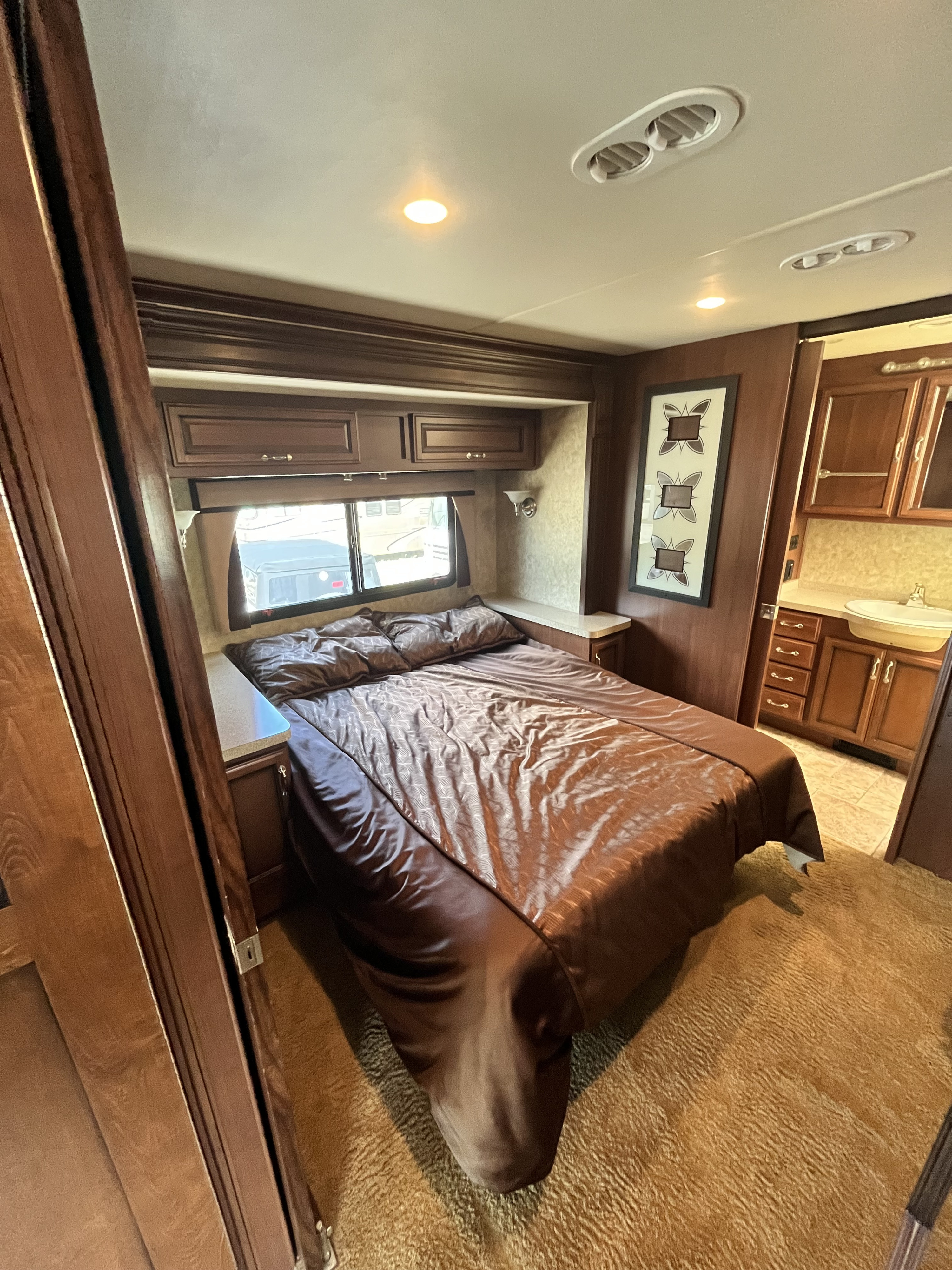 This RV rental bedroom features a large bed, built-in storage, and an attached compact vanity sink area with wood cabinets.. Fleetwood Bounder 2013