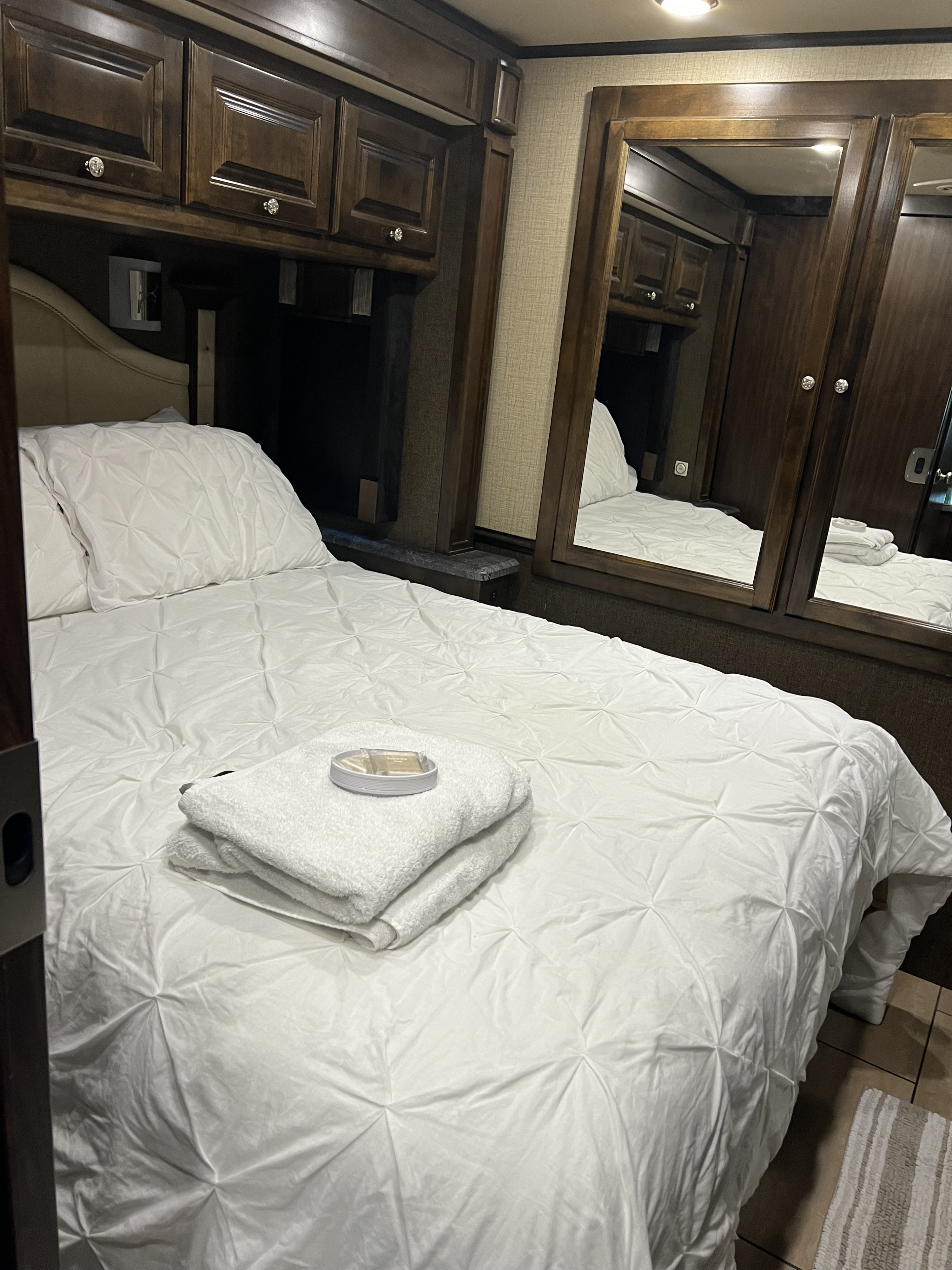 Cozy RV rental bedroom with clean white bedding, plump pillows, stacked towels & toiletries. Dark wood cabinets above.. Allegro Allegro Motorhome 2016