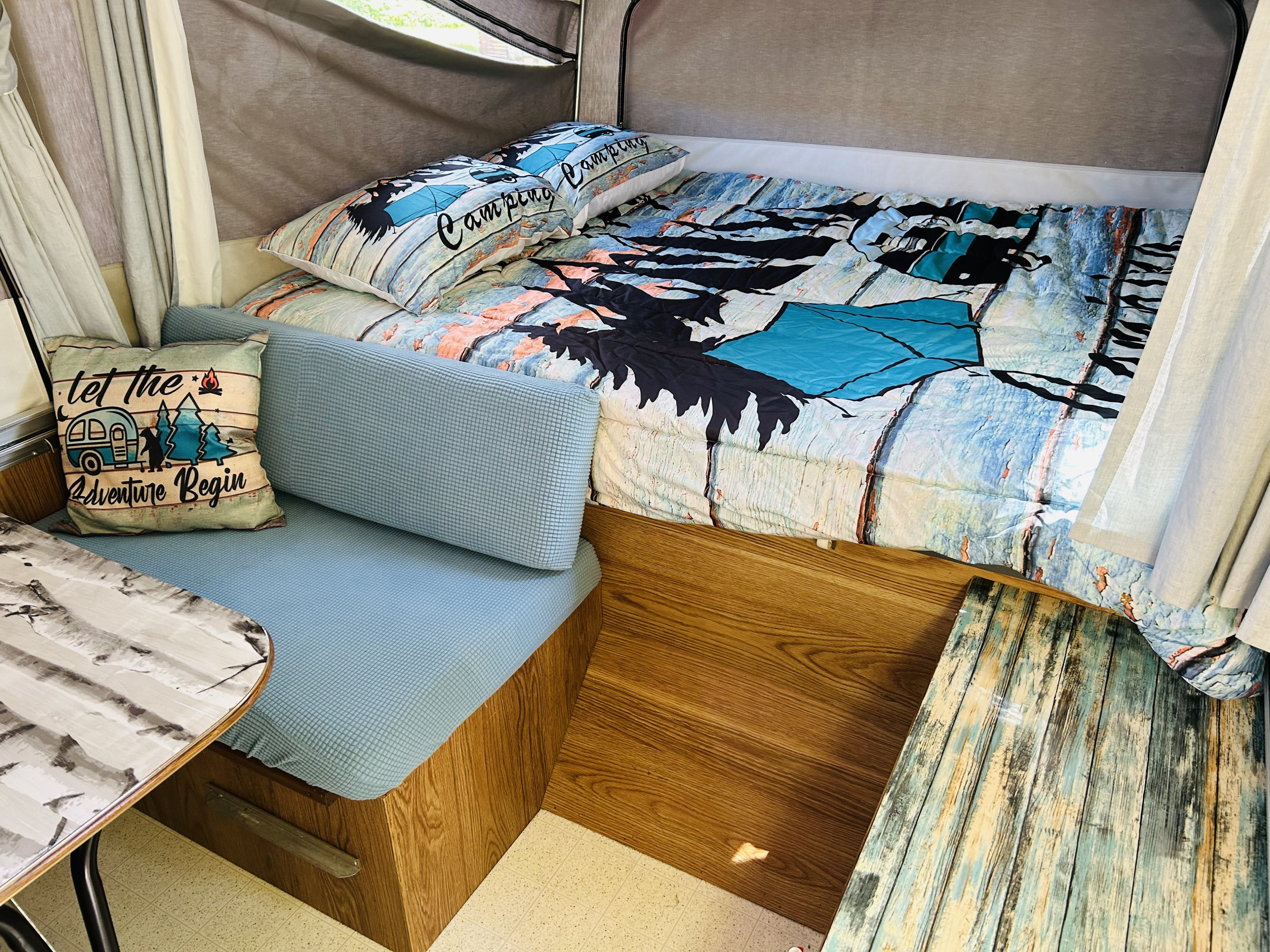 Cozy rv rental interior: bed with 'Camping' pillows, blue cushioned seating, & 'Adventure' pillow. Ready for your trip!. Cobra Flagstaff 1995