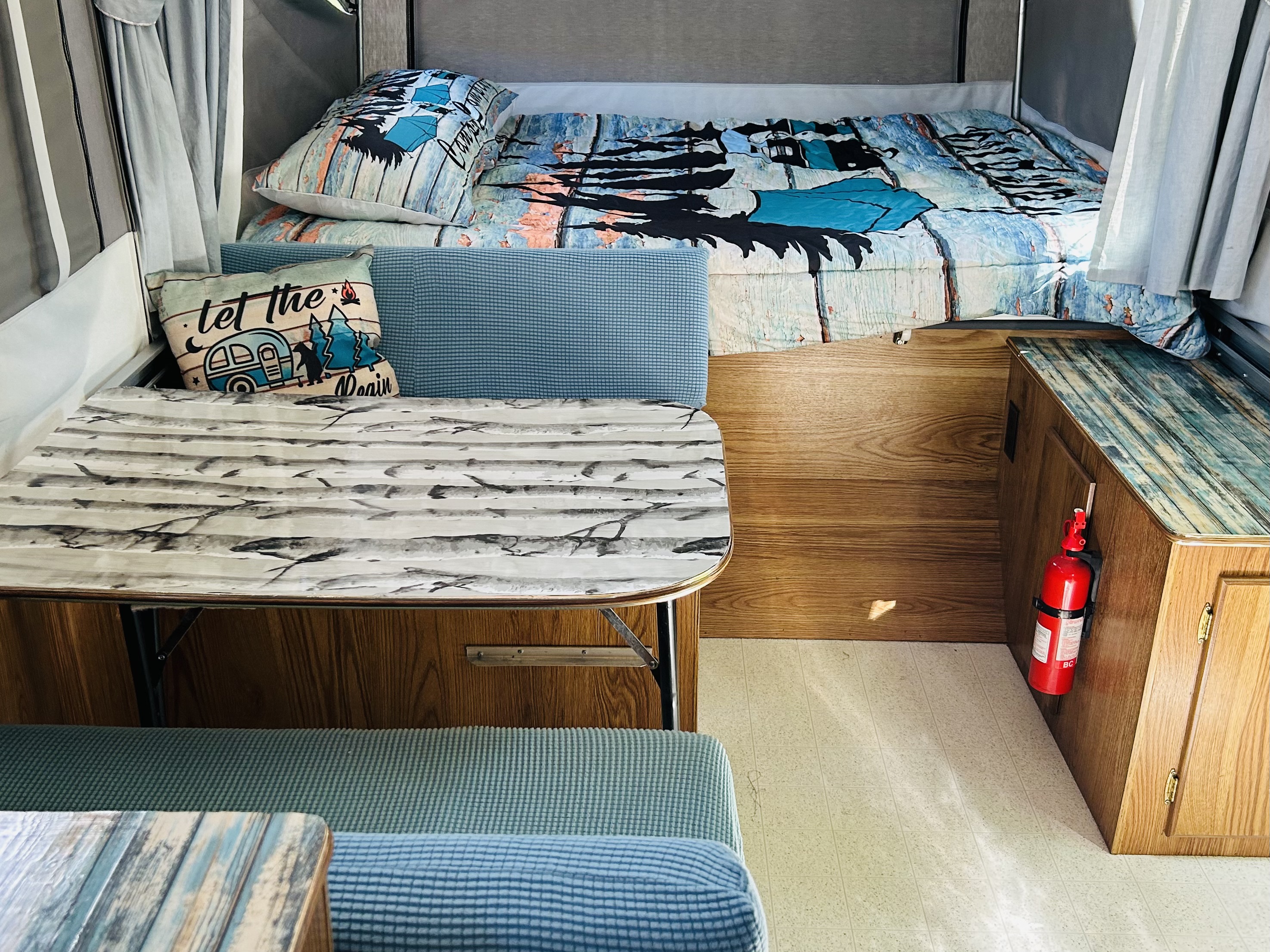 "Let the adventure begin" in this cozy RV rental, featuring a bed, dinette with patterned table, and blue seating.. Cobra Flagstaff 1995