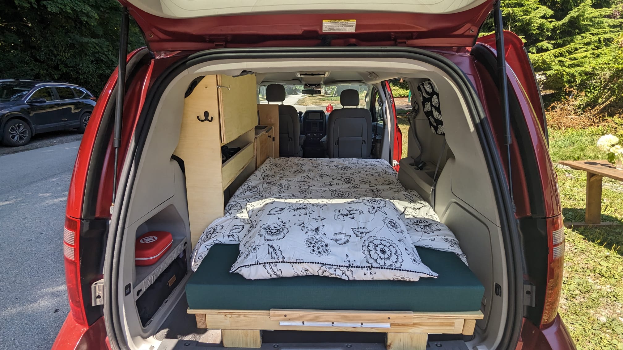 Red minivan converted to an RV rental, featuring a comfortable bed and storage unit inside. Ideal for road trips.. Dodge Dodge Grand Caravan 2008