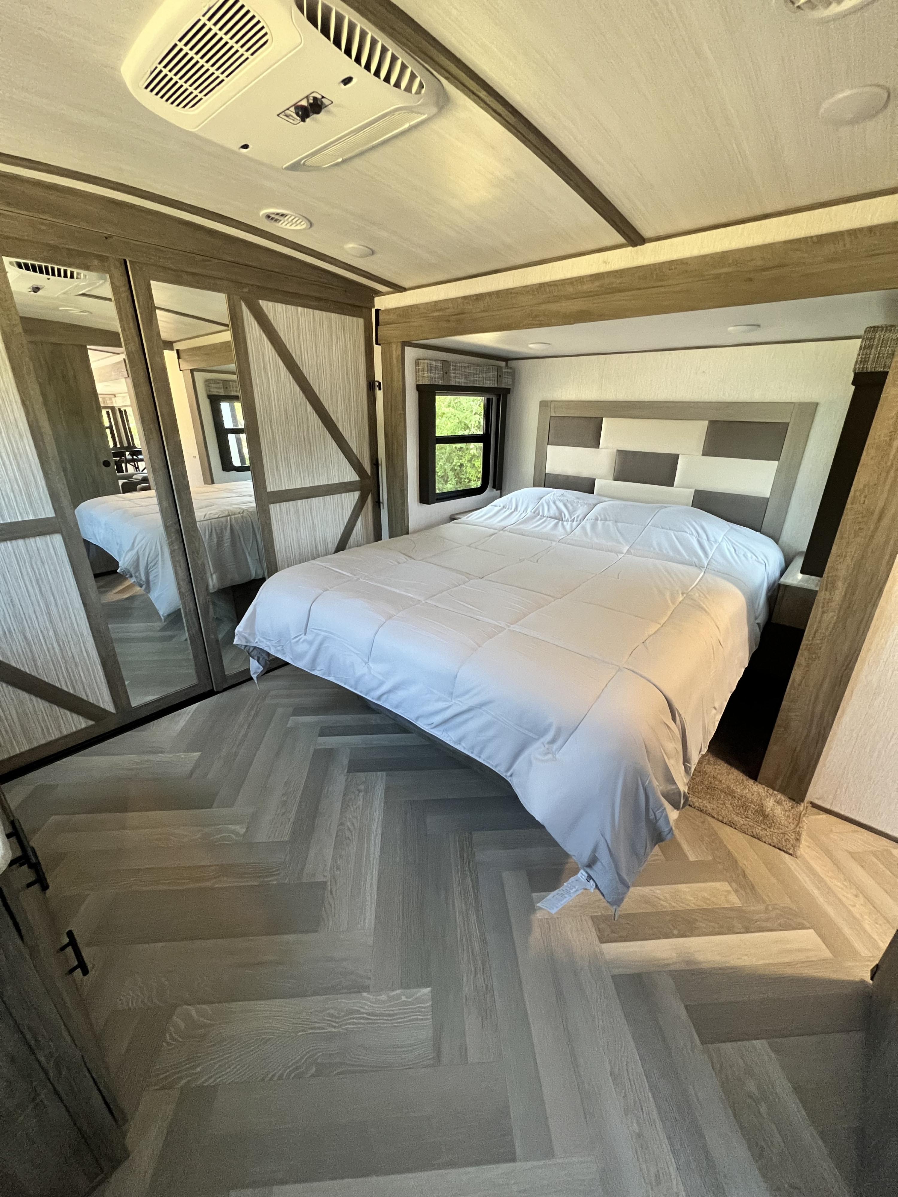 RV rental bedroom featuring a modern design, comfy bed, mirrored closet, and stylish herringbone flooring.. Forest River Salem Hemisphere 2022