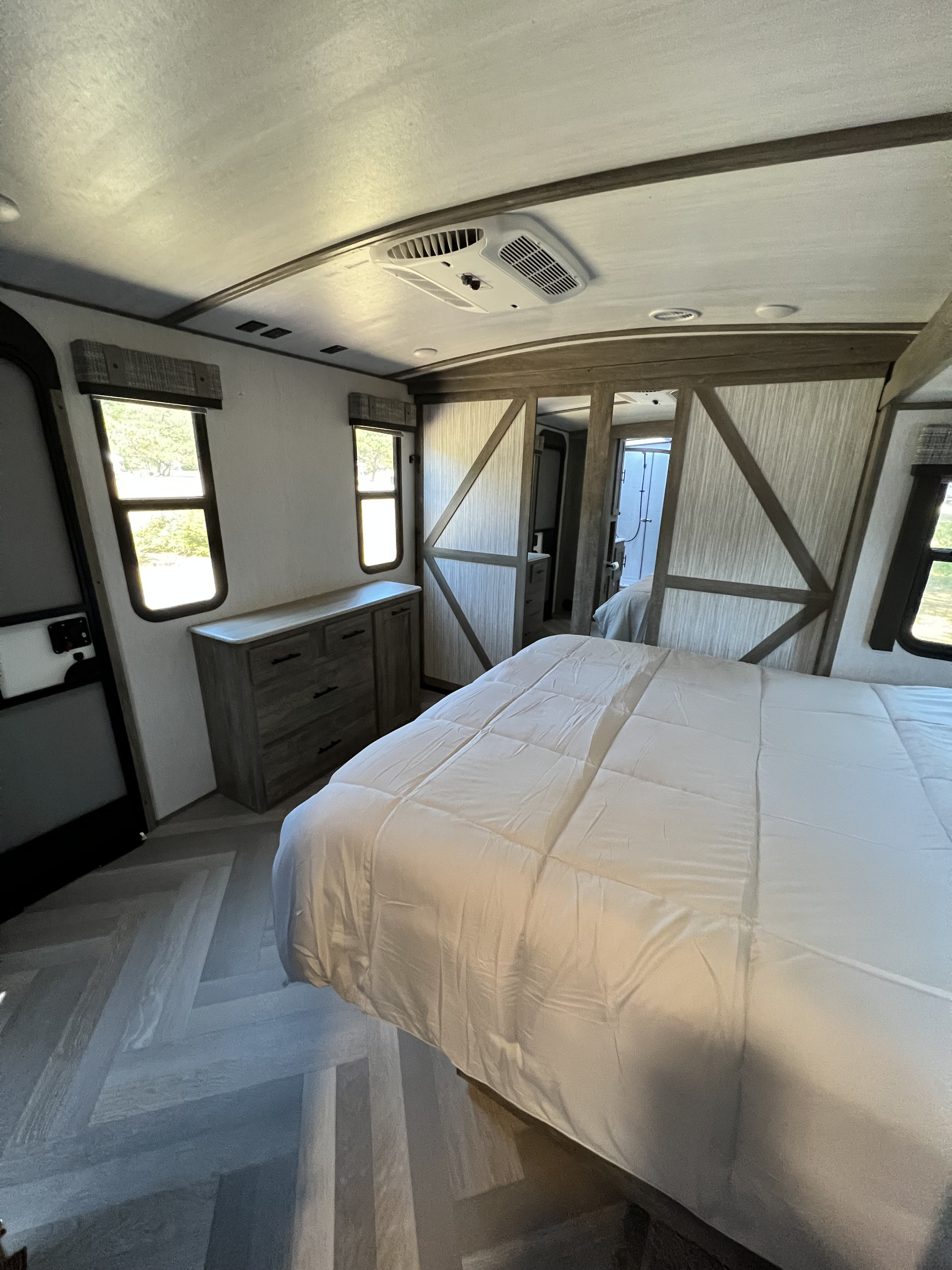 A bright and modern RV rental bedroom featuring a clean bed, dresser, two windows, AC unit, and stylish sliding door.. Forest River Salem Hemisphere 2022