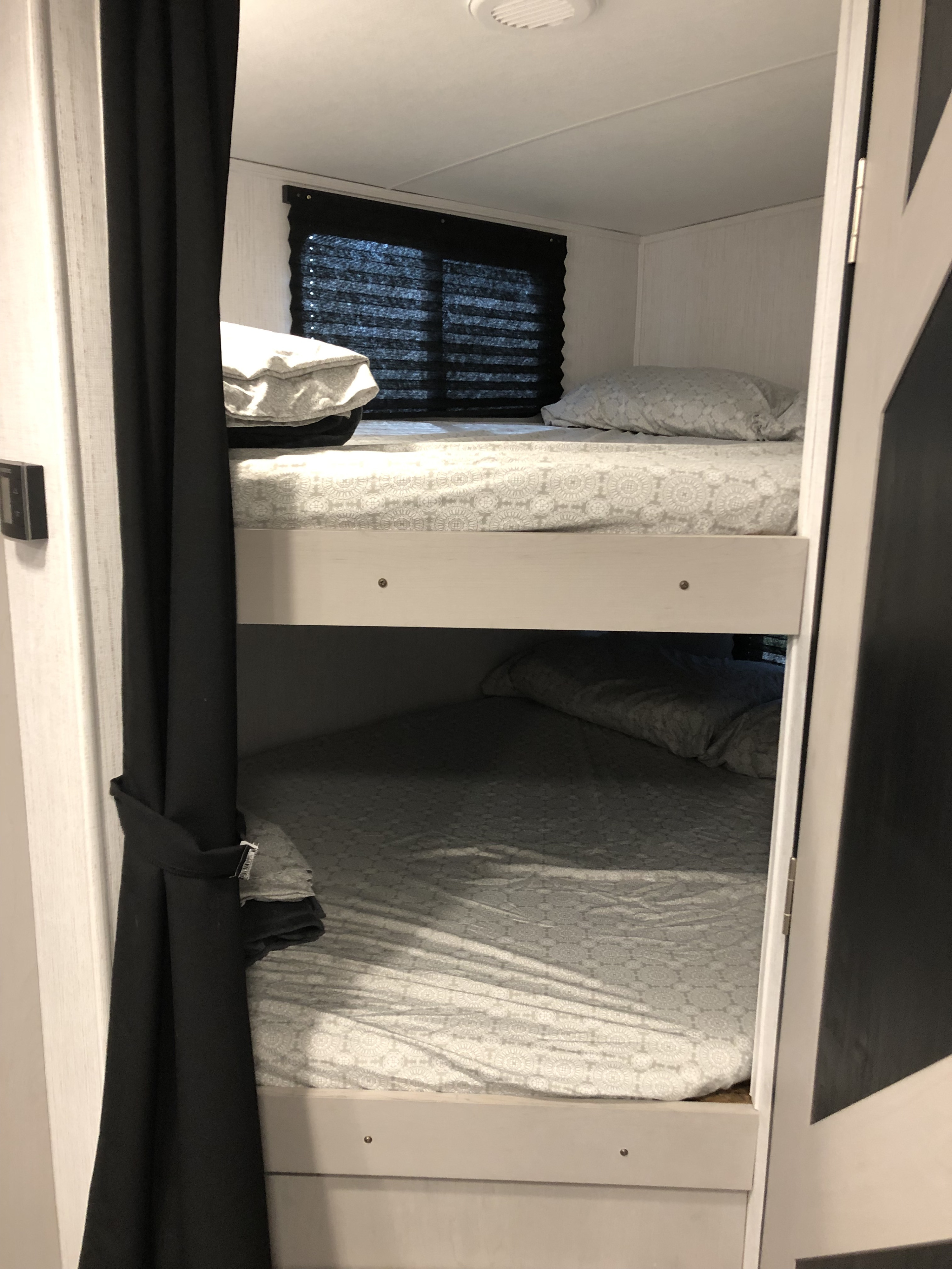 Cozy bunk beds in an RV rental, featuring light gray patterned sheets, pillows, and window blinds for comfortable sleeping.. Heartland RVs Mallard 2023