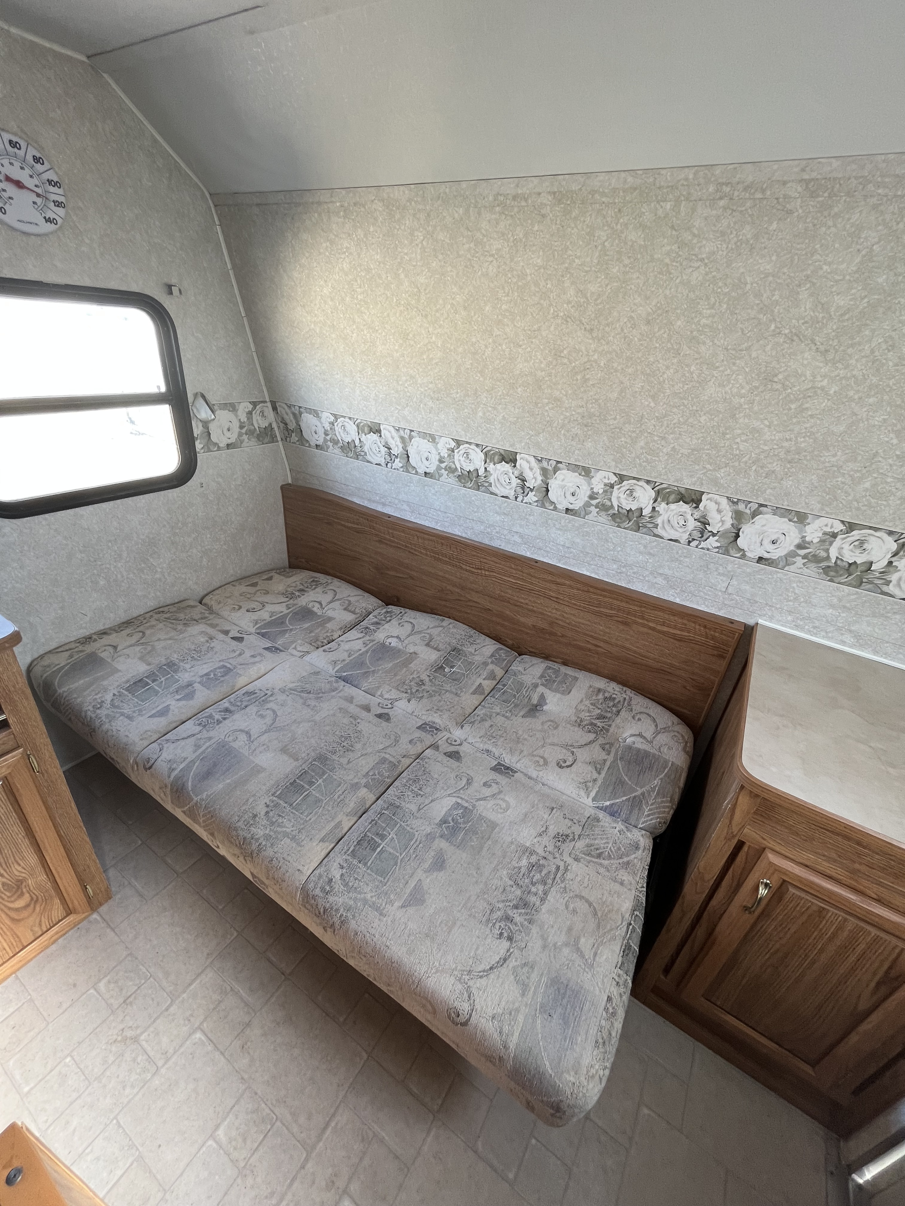 Cozy RV rental interior with a cushioned bench bed, wood cabinets, a window, and a wall thermometer.. Pioneer Pioneer Trailer 2004
