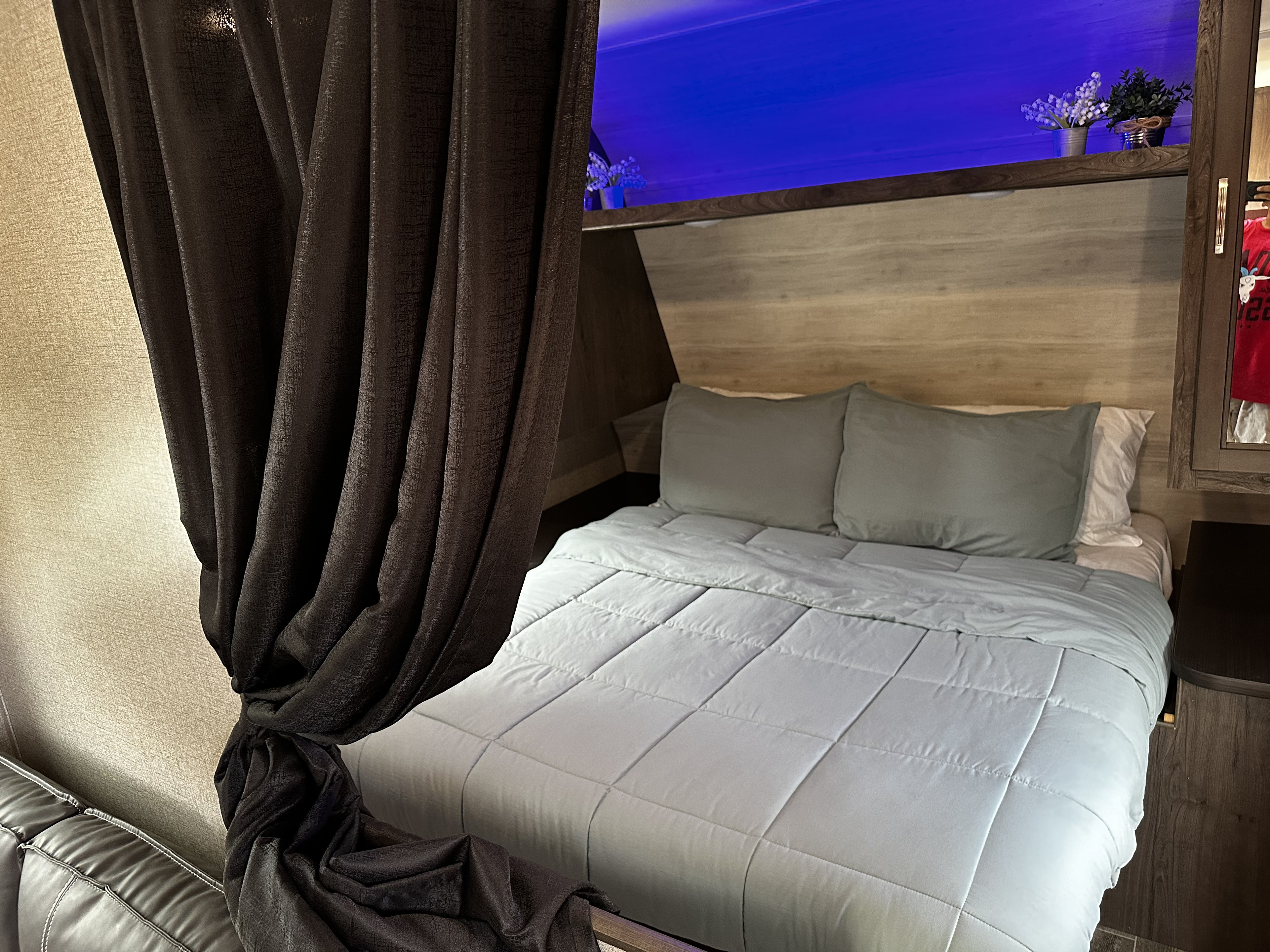 Experience comfort in this RV rental bedroom featuring a cozy bed, vibrant blue lighting, and dark privacy curtains.. Jayco Jay Flight SLX Rocky Mountain Edition 2021