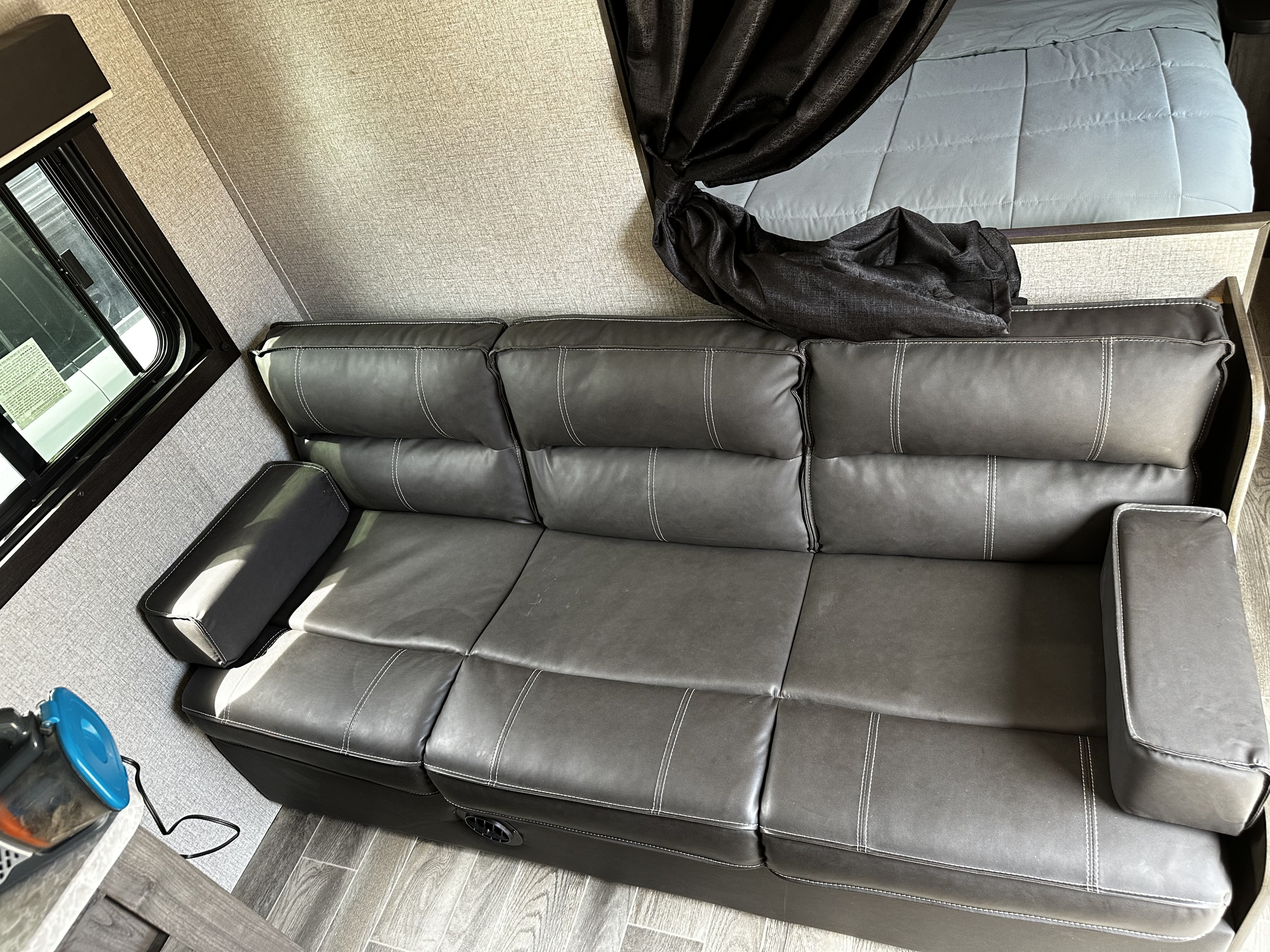 RV rental interior: A dark grey sofa with white stitching, light blue bed, and window in a compact living area.. Jayco Jay Flight SLX Rocky Mountain Edition 2021