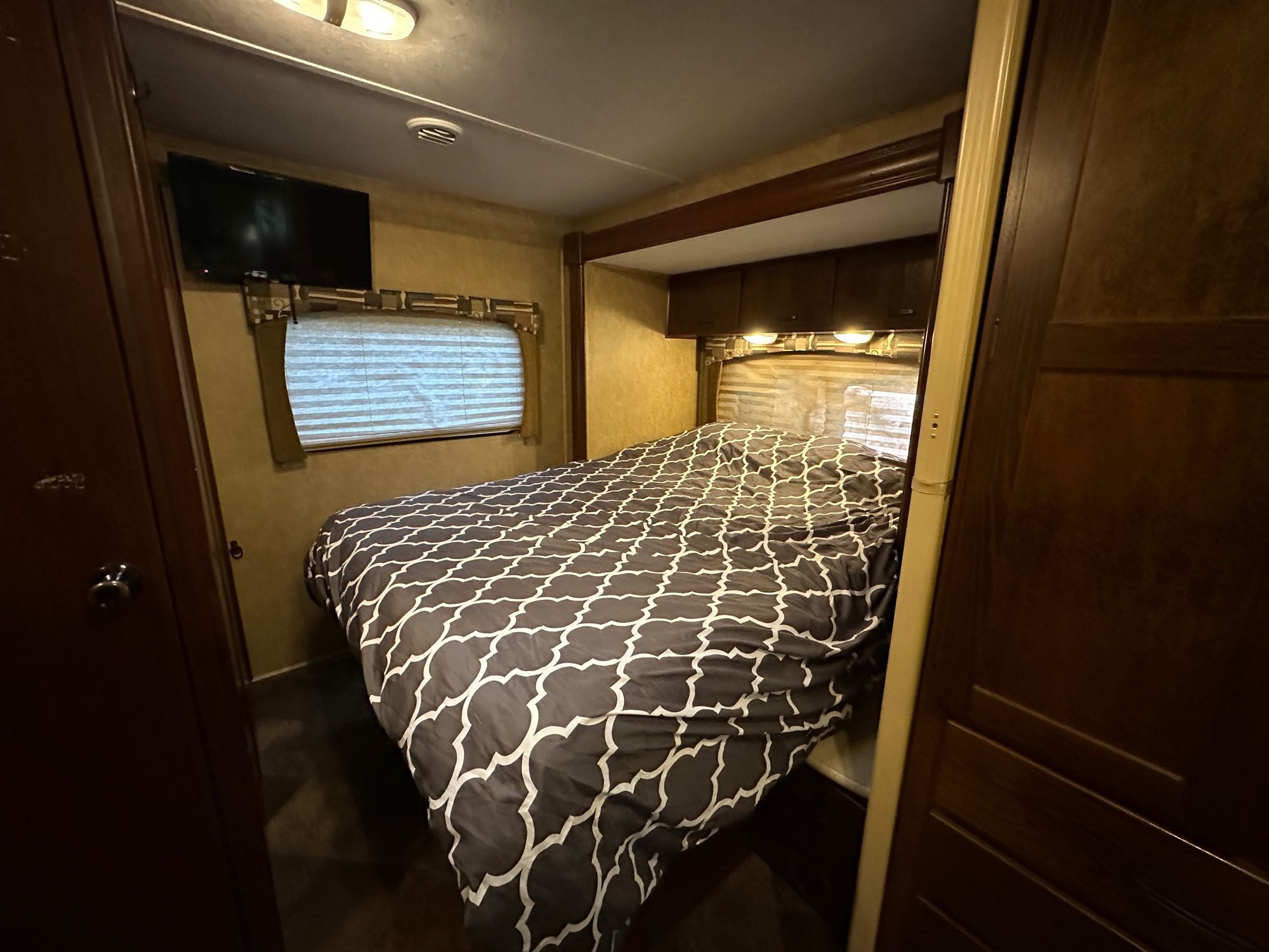 An inviting RV rental bedroom featuring a bed, mounted TV, and built-in storage.. Forest River Chevy Express 2014