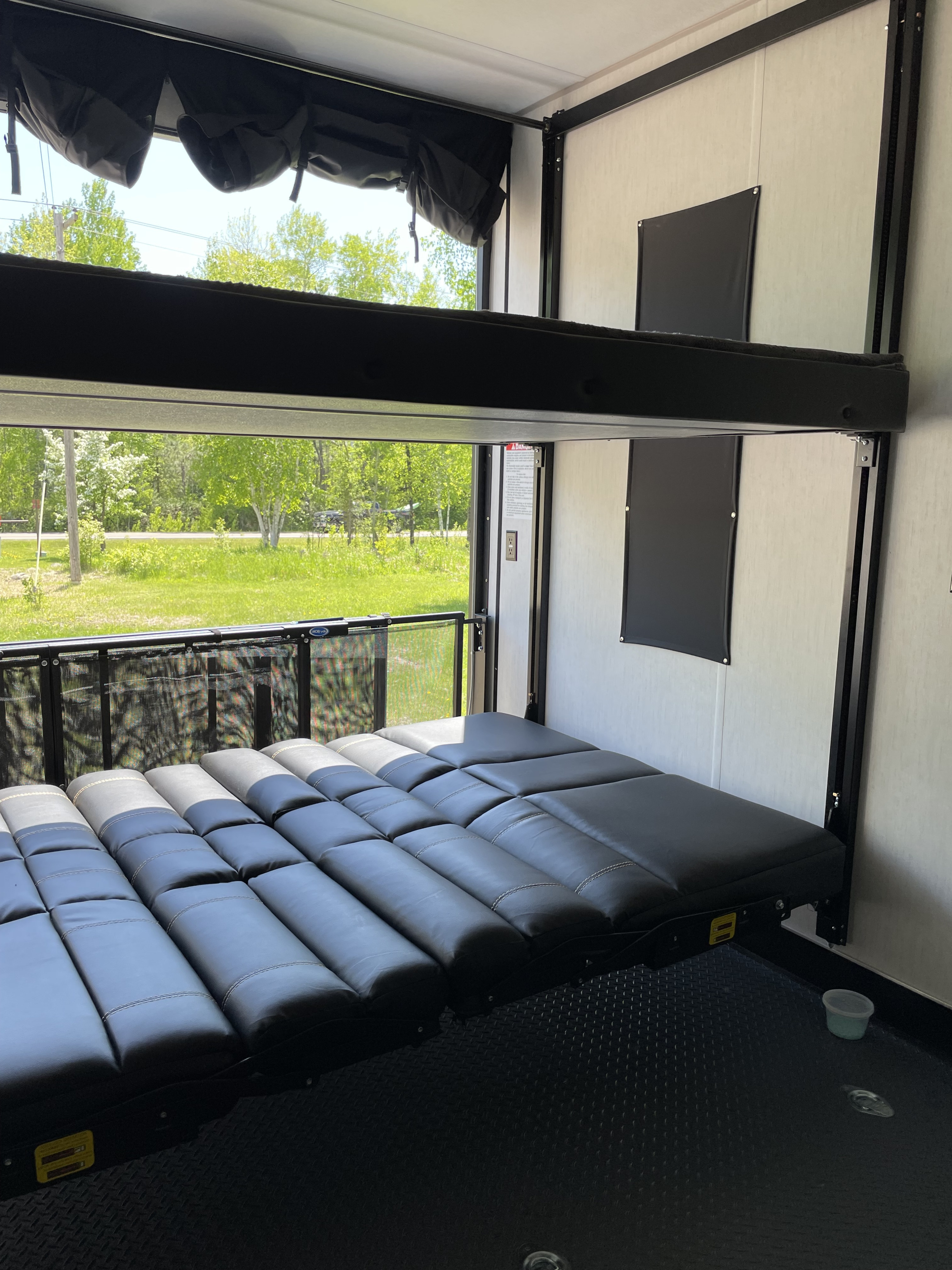 Inside an RV rental toy hauler, showing convertible bunks (lower bed, upper stowed), open ramp, and outdoor view.. Forest River Cherokee Wolf Pack 2020