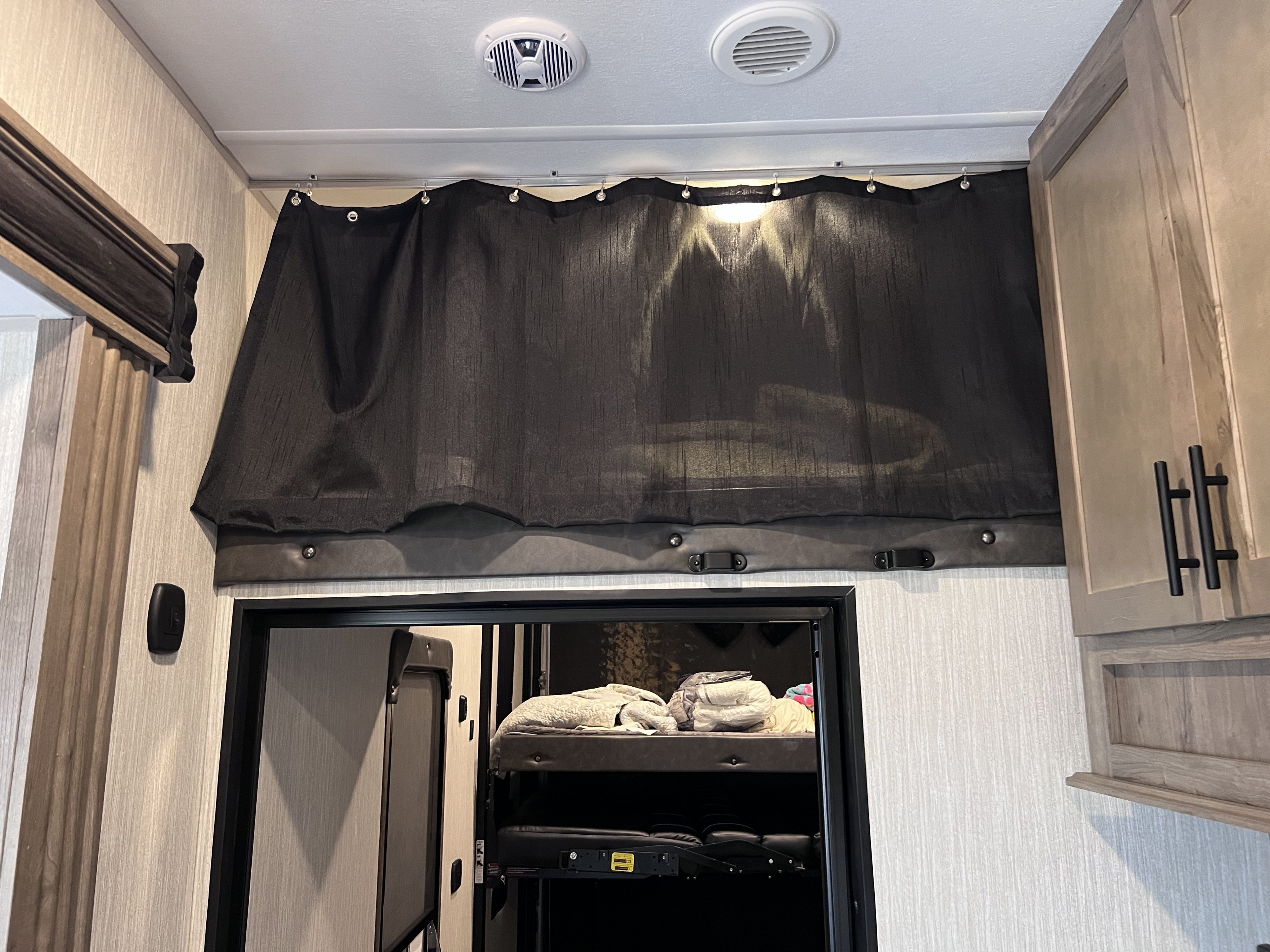 Inside an RV rental: a dark privacy curtain covers an upper bunk area, with visible ceiling vents, offering cozy mobile living.. Forest River Cherokee Wolf Pack 2020
