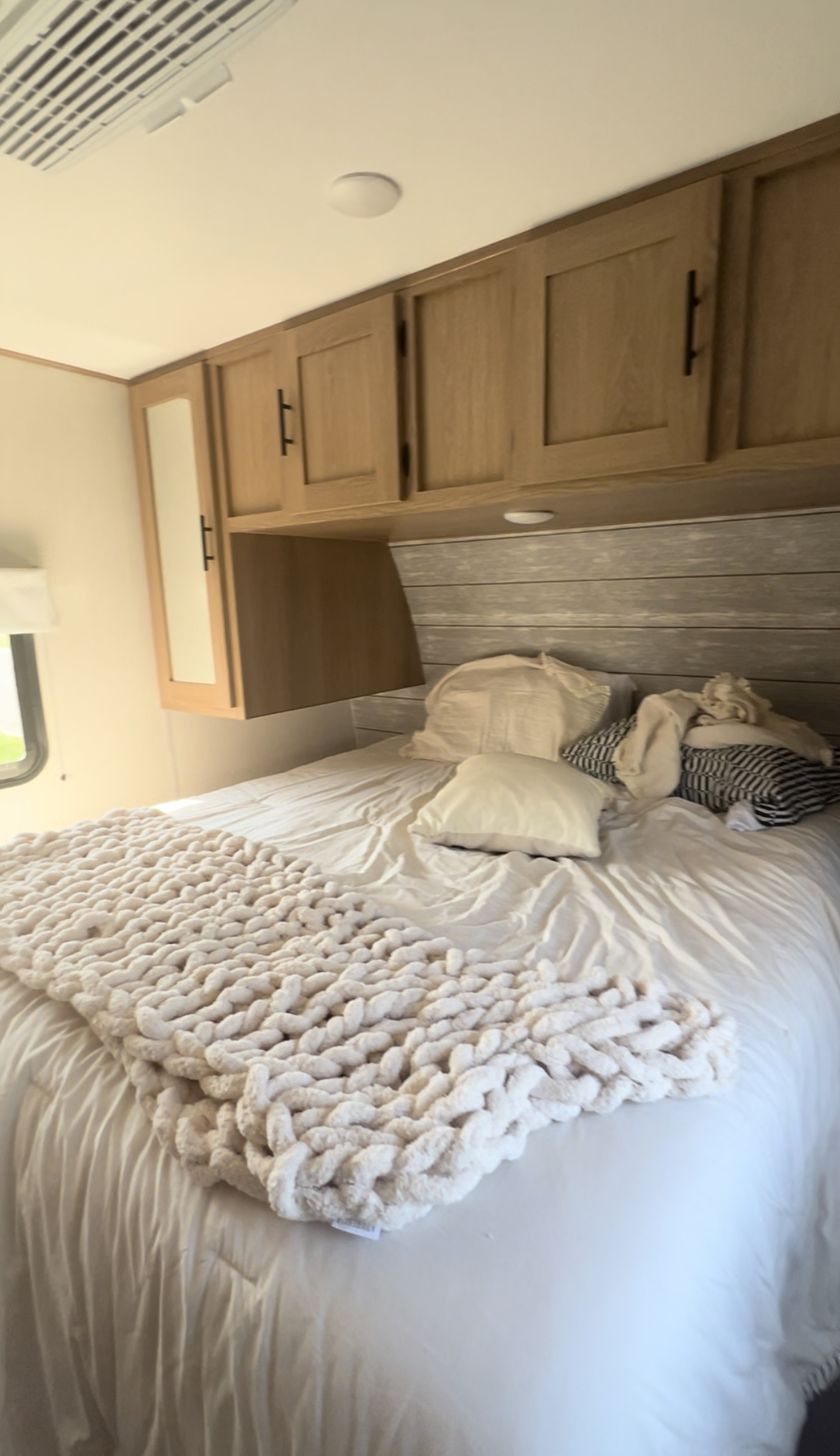 Cozy RV rental bedroom with a bed, chunky knit blanket, and wooden overhead cabinets for storage.. Other Other 2023
