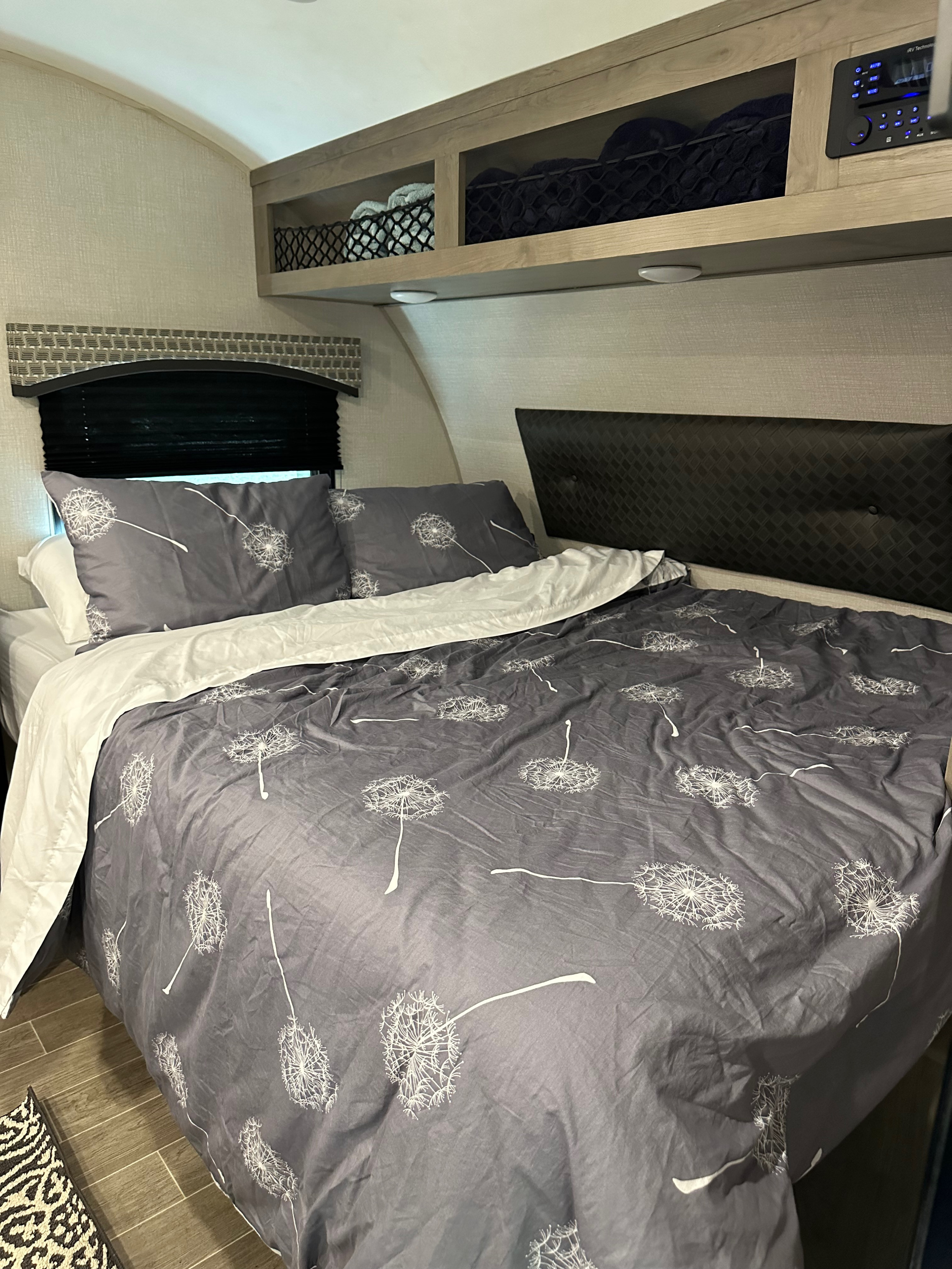 Cozy RV rental bedroom features a bed with dandelion duvet, headboard, storage, and control panel for a comfortable stay.. Venture Sonic Lite 2021