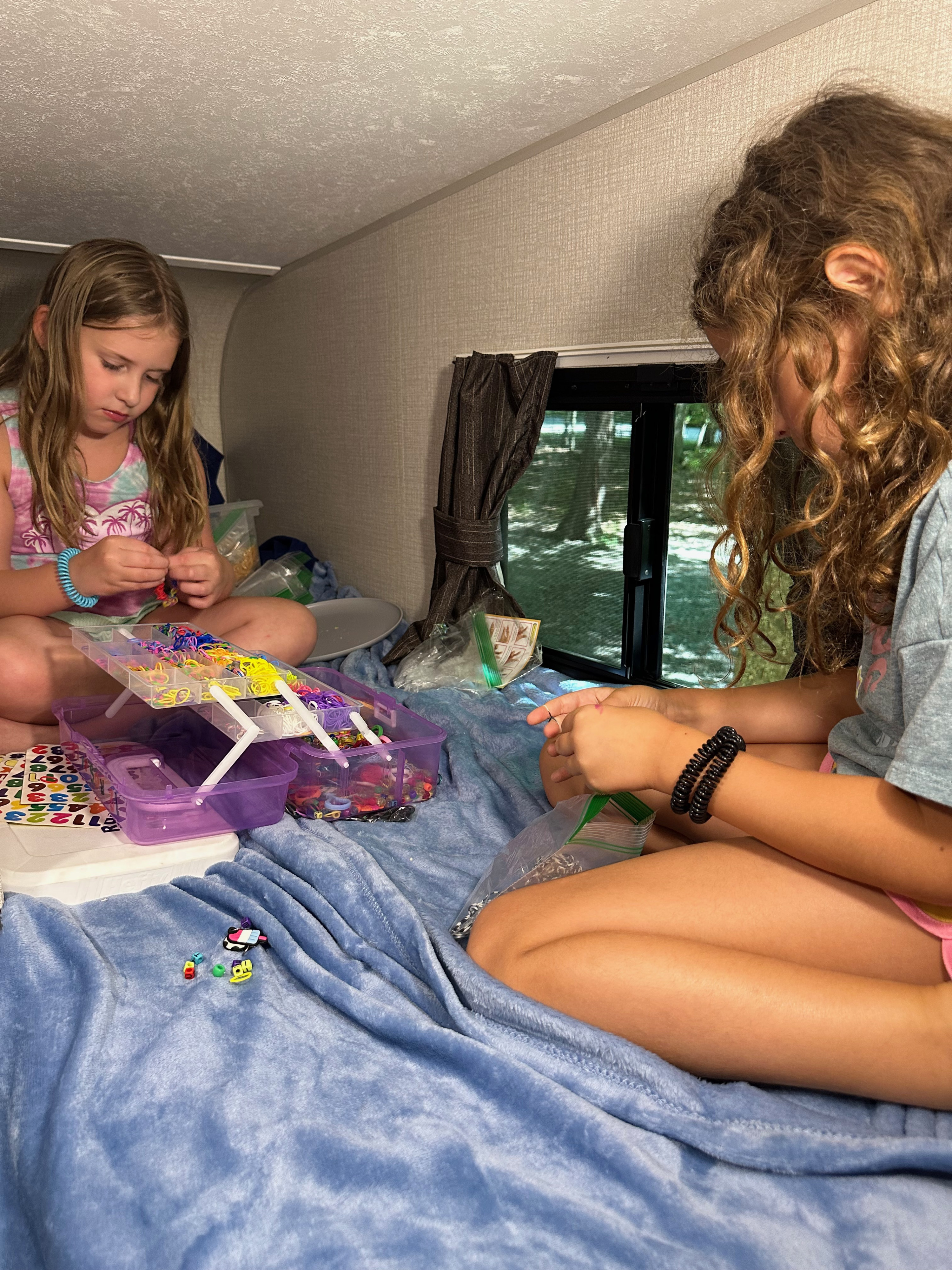 Two girls enjoy crafting colorful bracelets in a cozy RV rental, perfect for a camping trip activity.. Venture Sonic Lite 2021