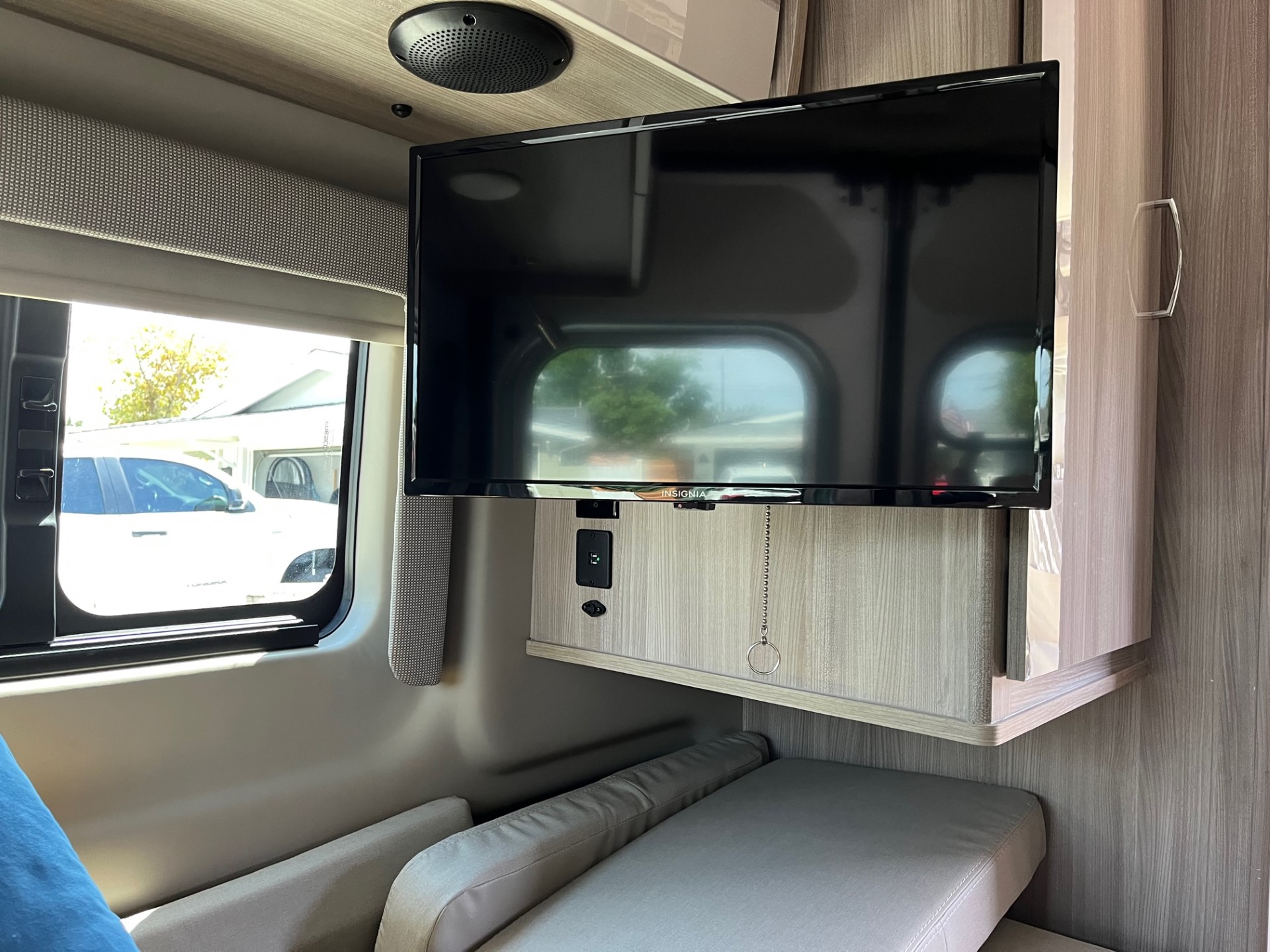 An RV rental interior showing a mounted Insignia TV, charging ports, and comfortable seating in the living area.. Thor Sequnce 2023