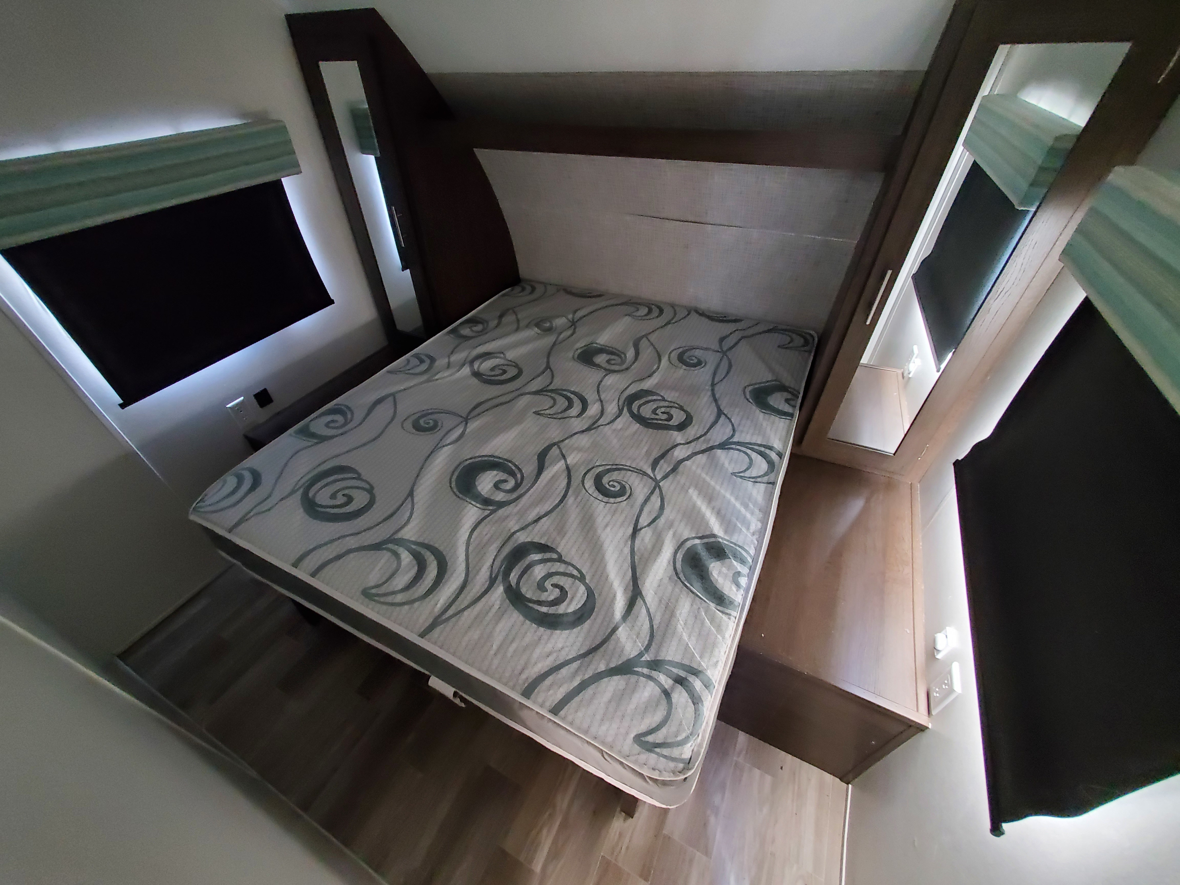 Cozy RV rental bedroom featuring a patterned mattress, compact side tables, windows, and built-in lighting.. Forest River Wildwood X-Lite 2020