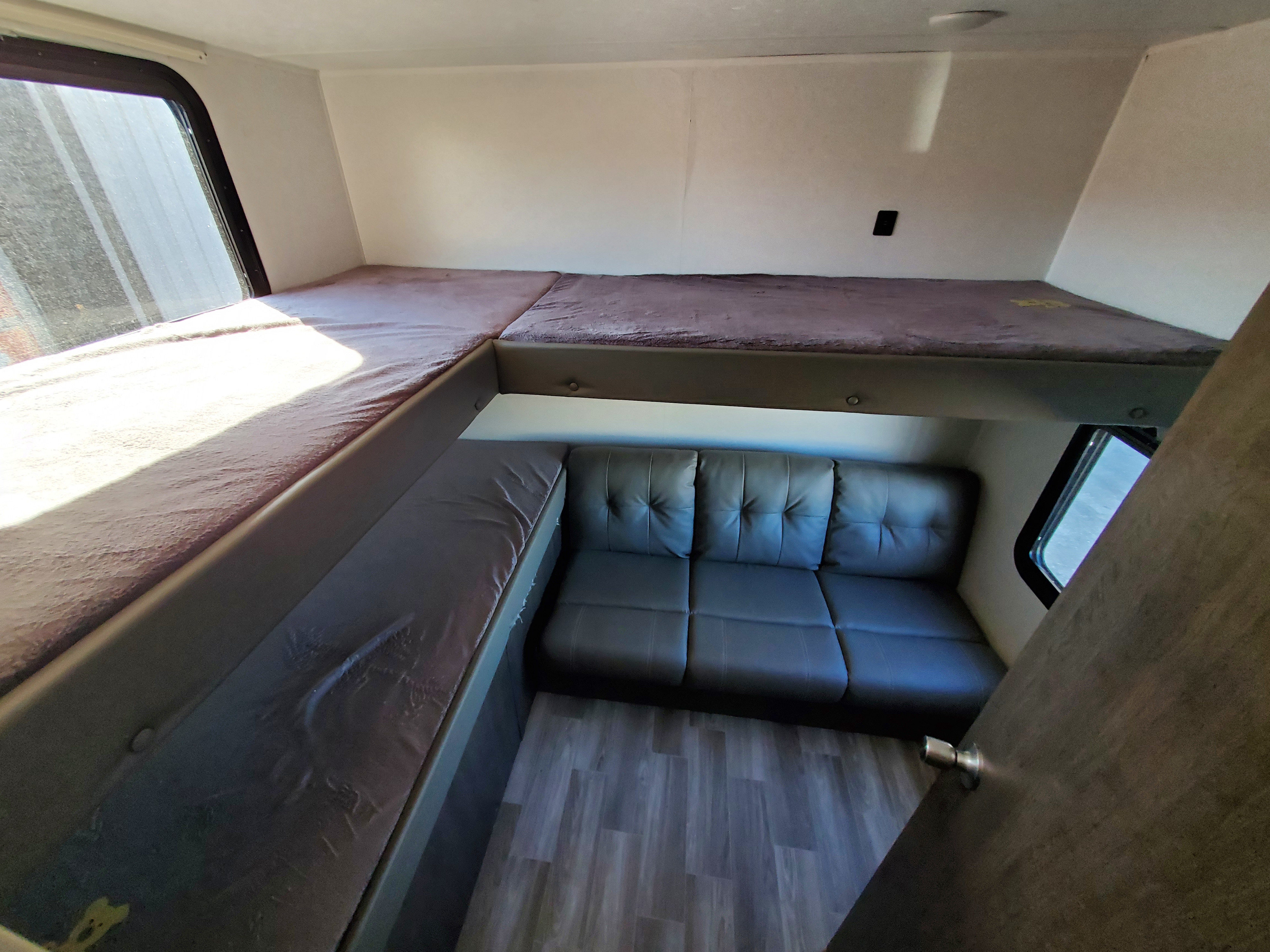 RV rental interior showcasing bunk beds over a grey sofa, light wood floor, and windows for natural light.. Forest River Wildwood X-Lite 2020