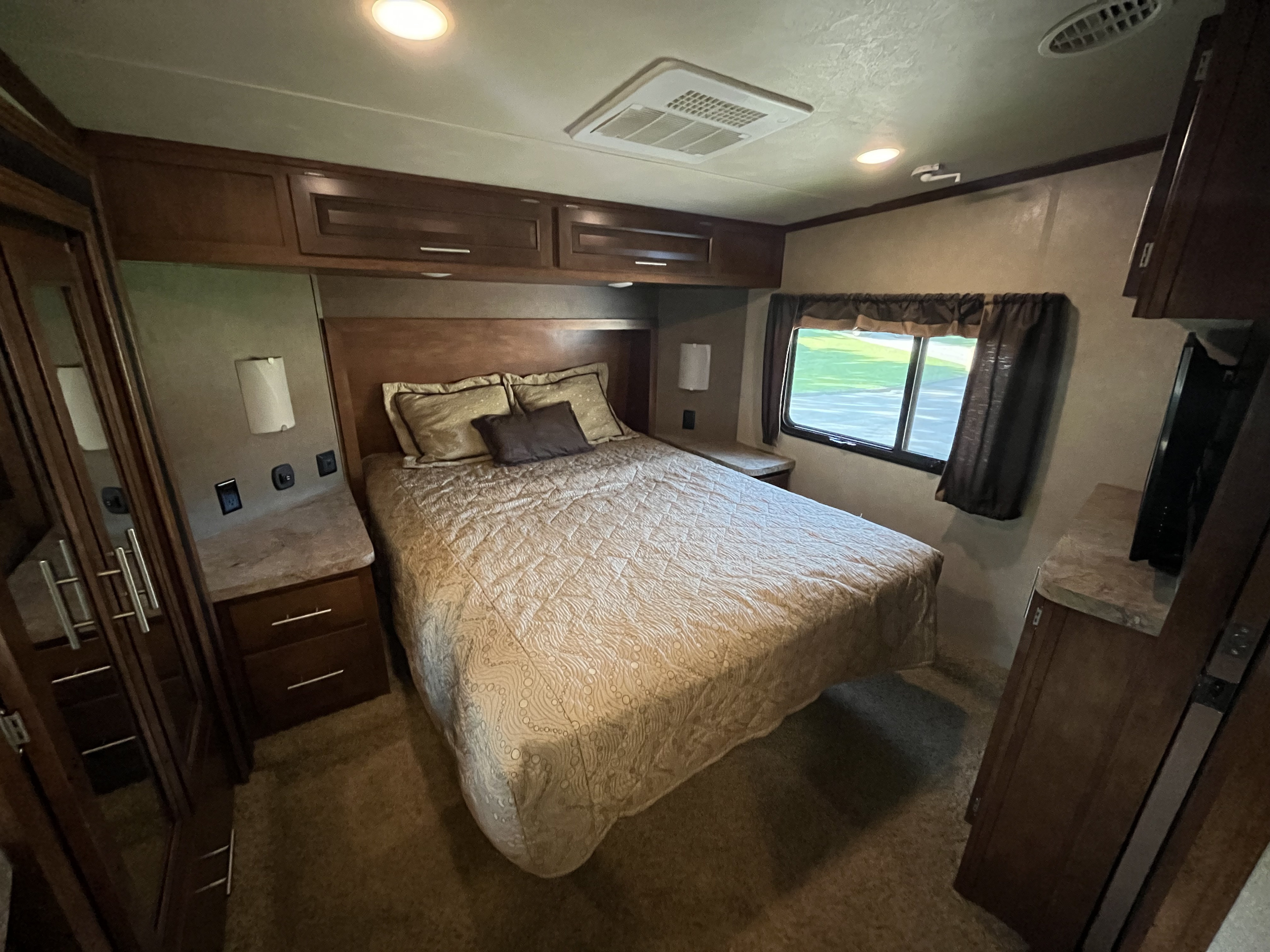Spacious RV rental bedroom with a comfy bed, dark wood cabinets, a large window, and cozy lighting for restful travel.. Forest River XLR Thunderbolt Toy Hauler 2015