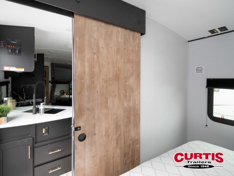 Modern RV rental interior: kitchen with sink, sliding door to bedroom, and comfy mattress. Ideal for compact travel trailer living.. Keystone RV Springdale 2023