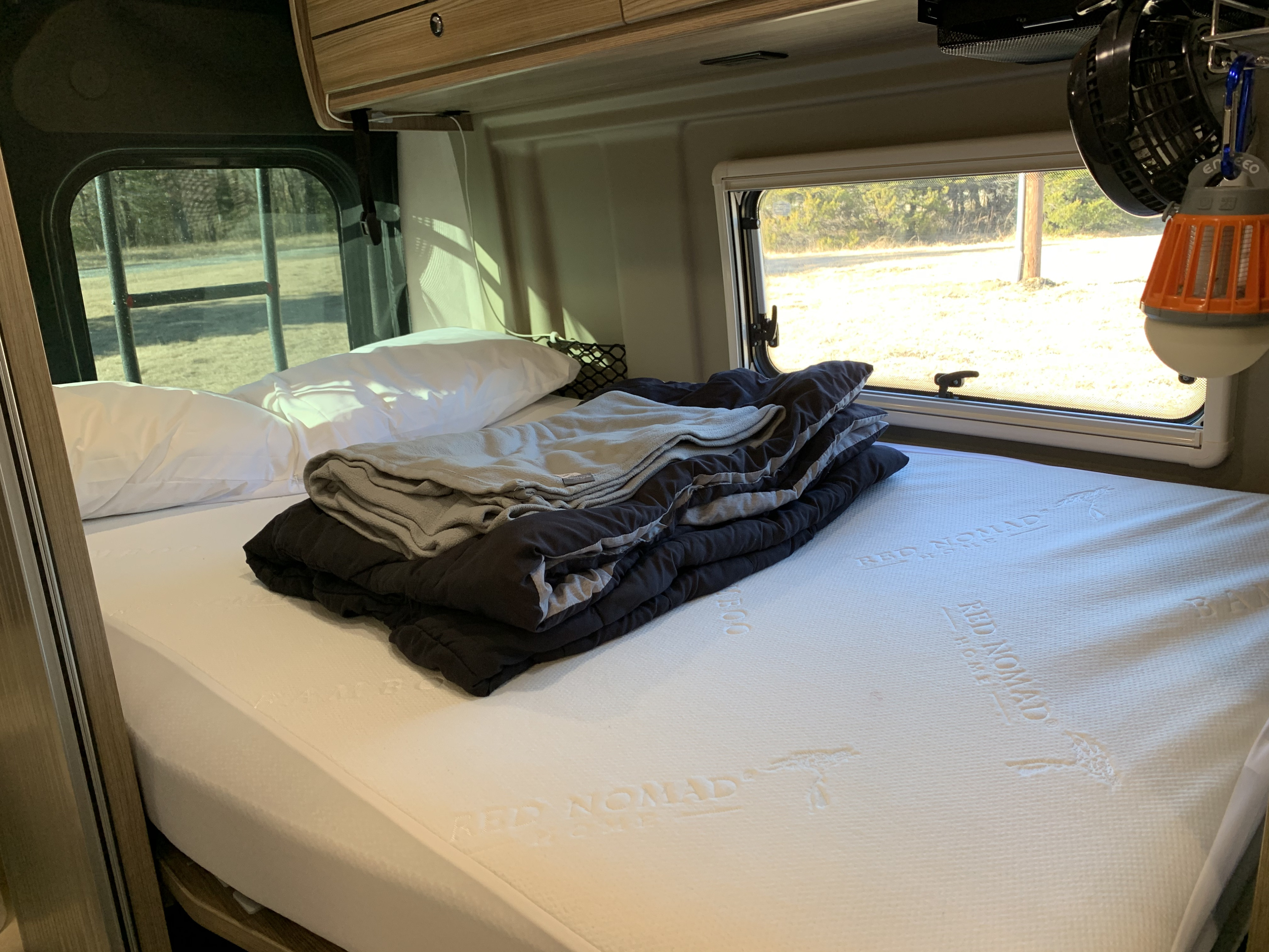 Comfortable RV rental bed with Red Nomad mattress, pillows, and blankets, promising restful sleep on your trip.. Winnebago Travato 2020