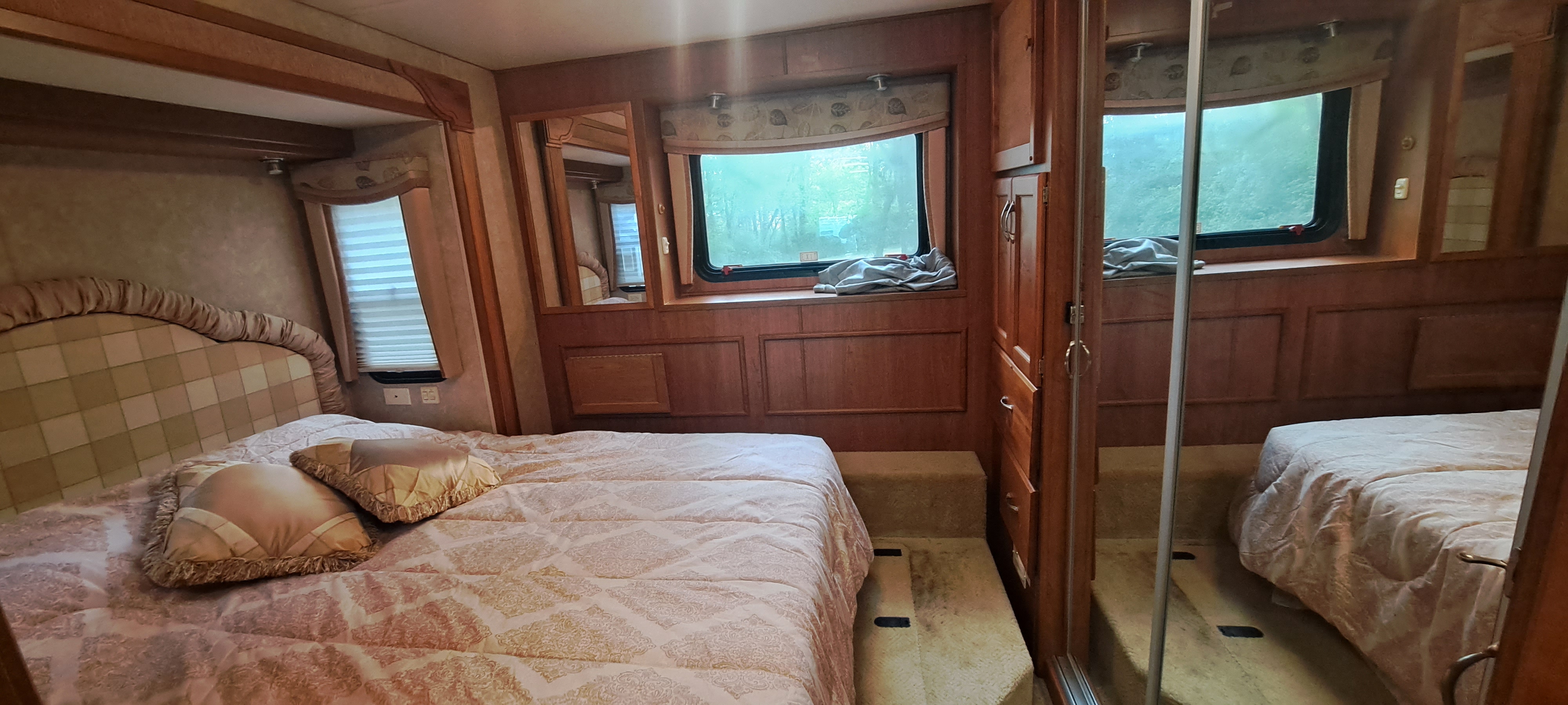 Spacious RV rental bedroom featuring a large bed, decorative headboard, windows, wood paneling, and a mirrored closet.. Monaco La Palma XL Diesel 2007