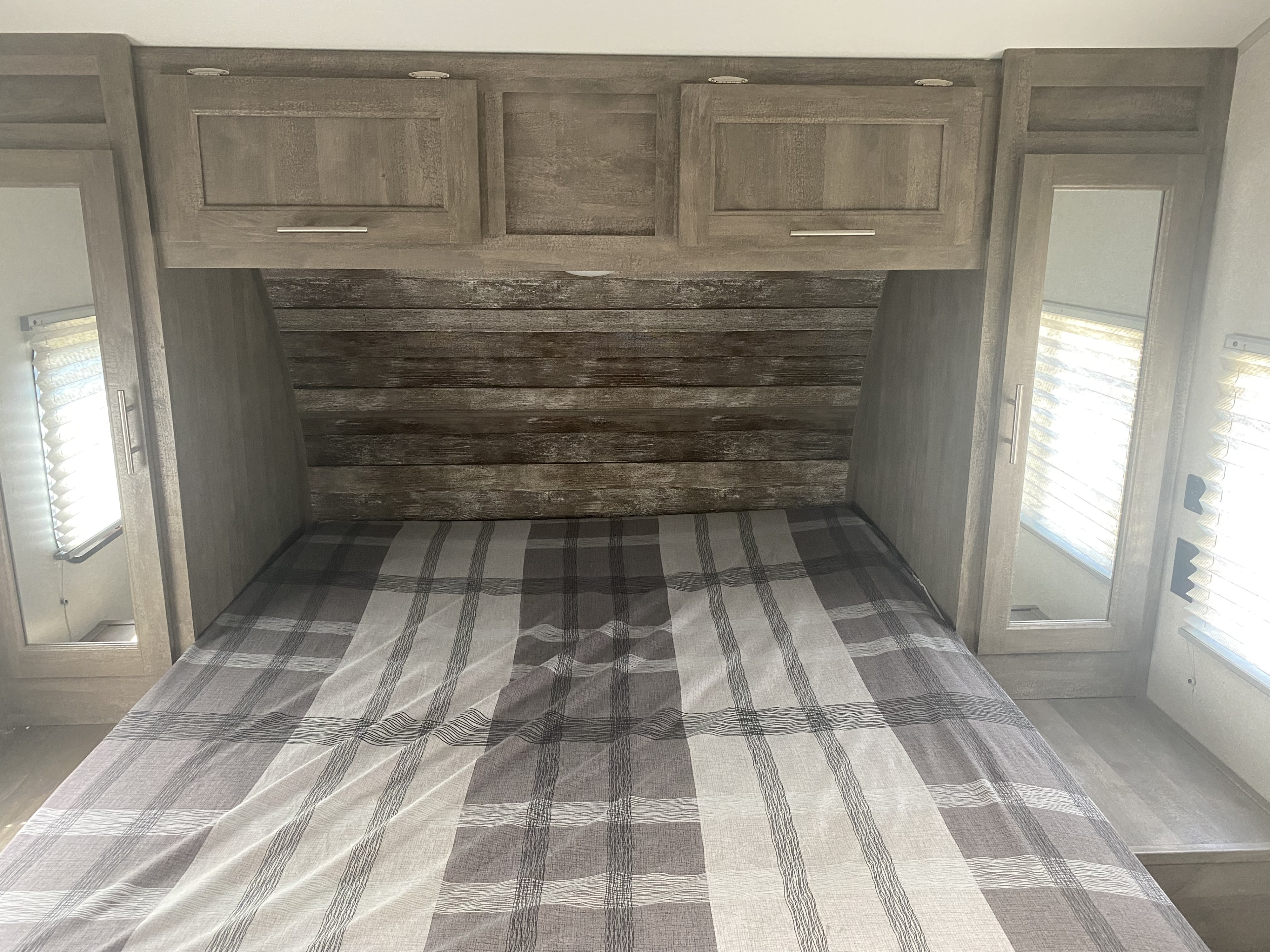 RV rental bedroom: cozy bed with plaid bedding, wood-toned overhead cabinets, and side storage for comfortable travel.. Forest River Nitro Xlr 2022