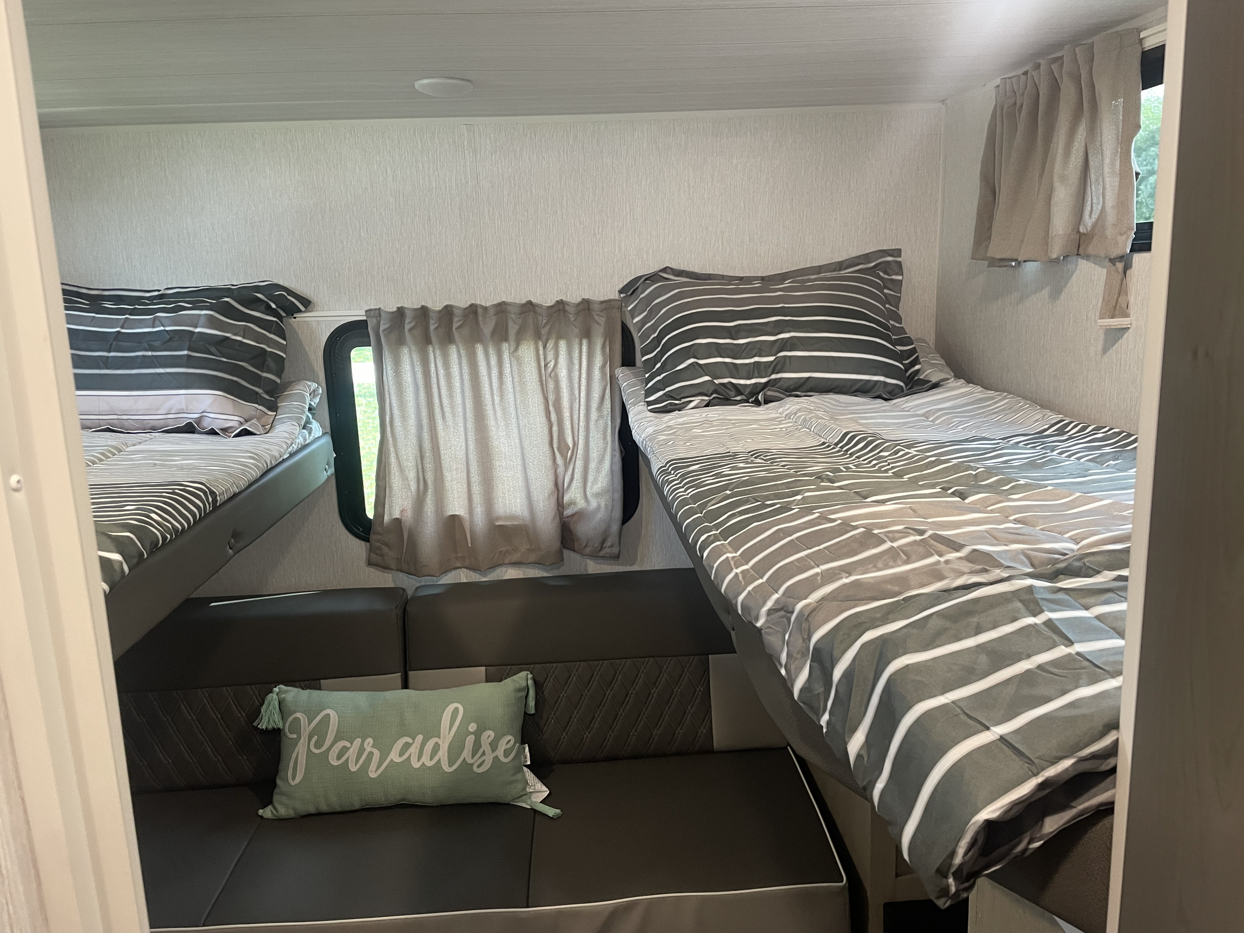 Cozy RV rental interior featuring comfortable bunk beds with striped bedding and a small seating area.. Forest River Wildwood X-Lite Platinum 2023