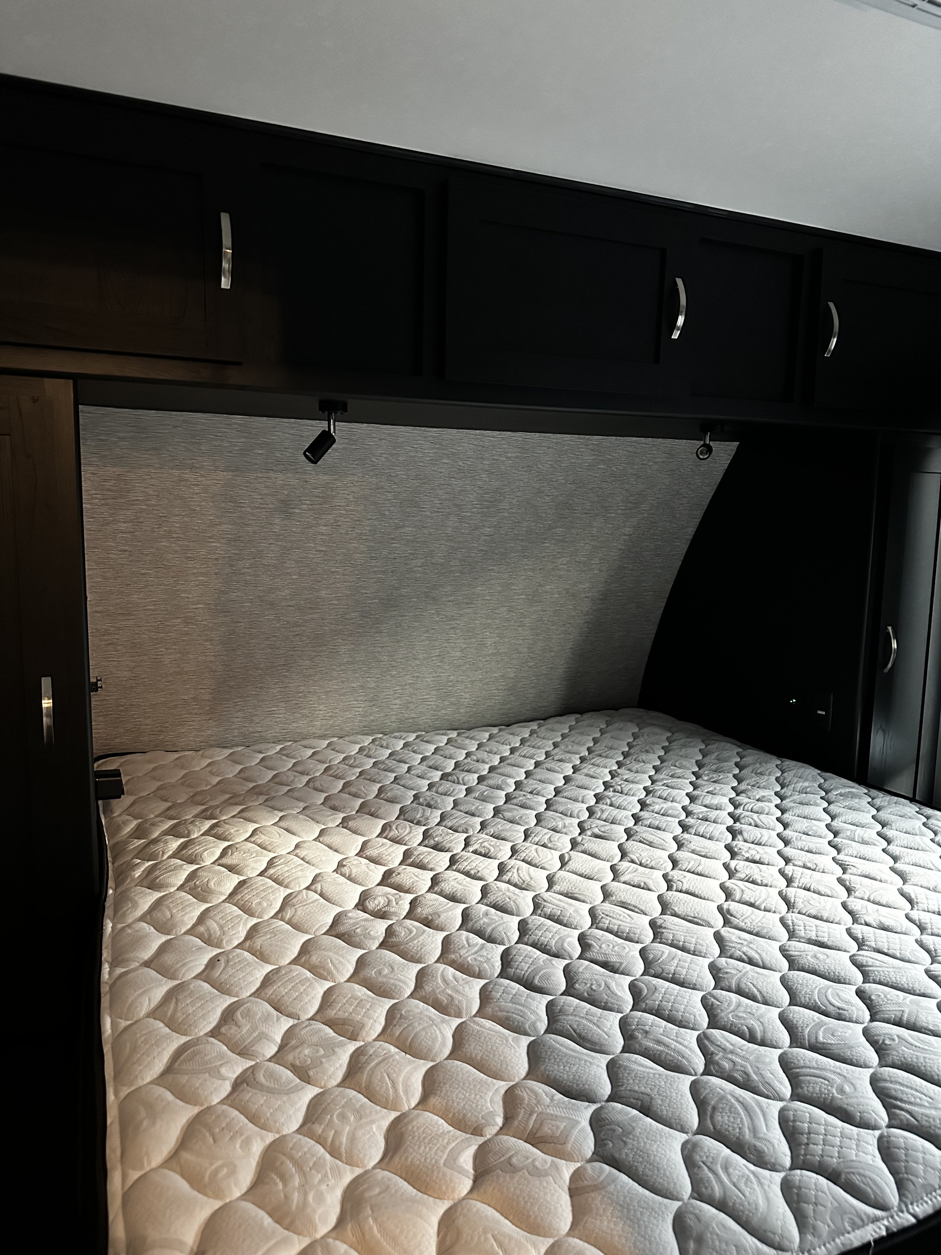 Well-appointed RV rental bedroom with a comfy quilted mattress, dark wood cabinetry, and ambient lighting above the bed.. Coachmen Adrenaline 2022