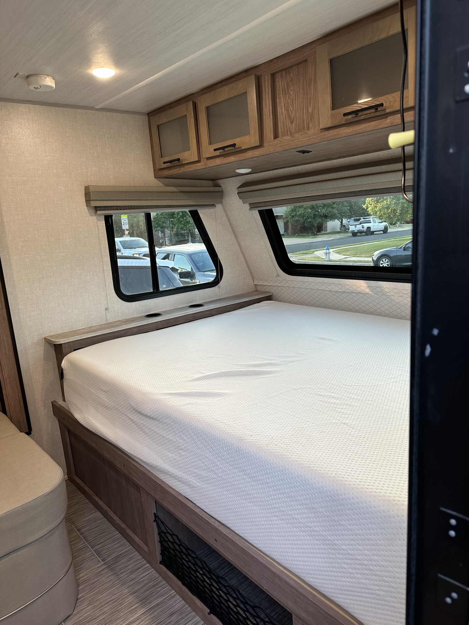 Cozy RV rental bedroom with a comfortable bed, overhead cabinets, and large windows revealing an outdoor street scene.. No Boundaries 19 2021