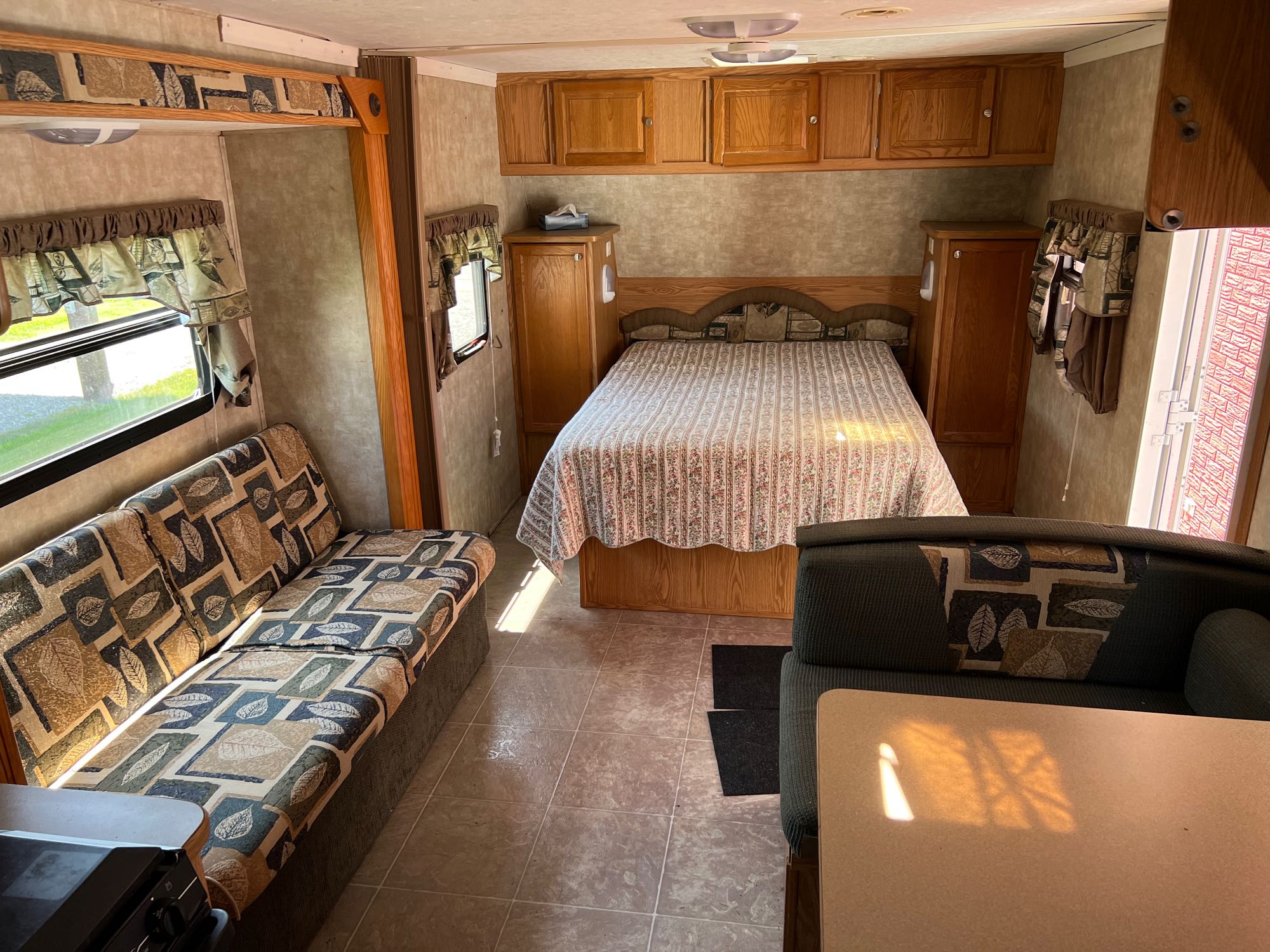 Inside an RV rental featuring a cozy bed, ample wood cabinets, and a patterned sofa. Ideal for travel.. Pilgrim International Inc Cirrus 24 CRB 2006