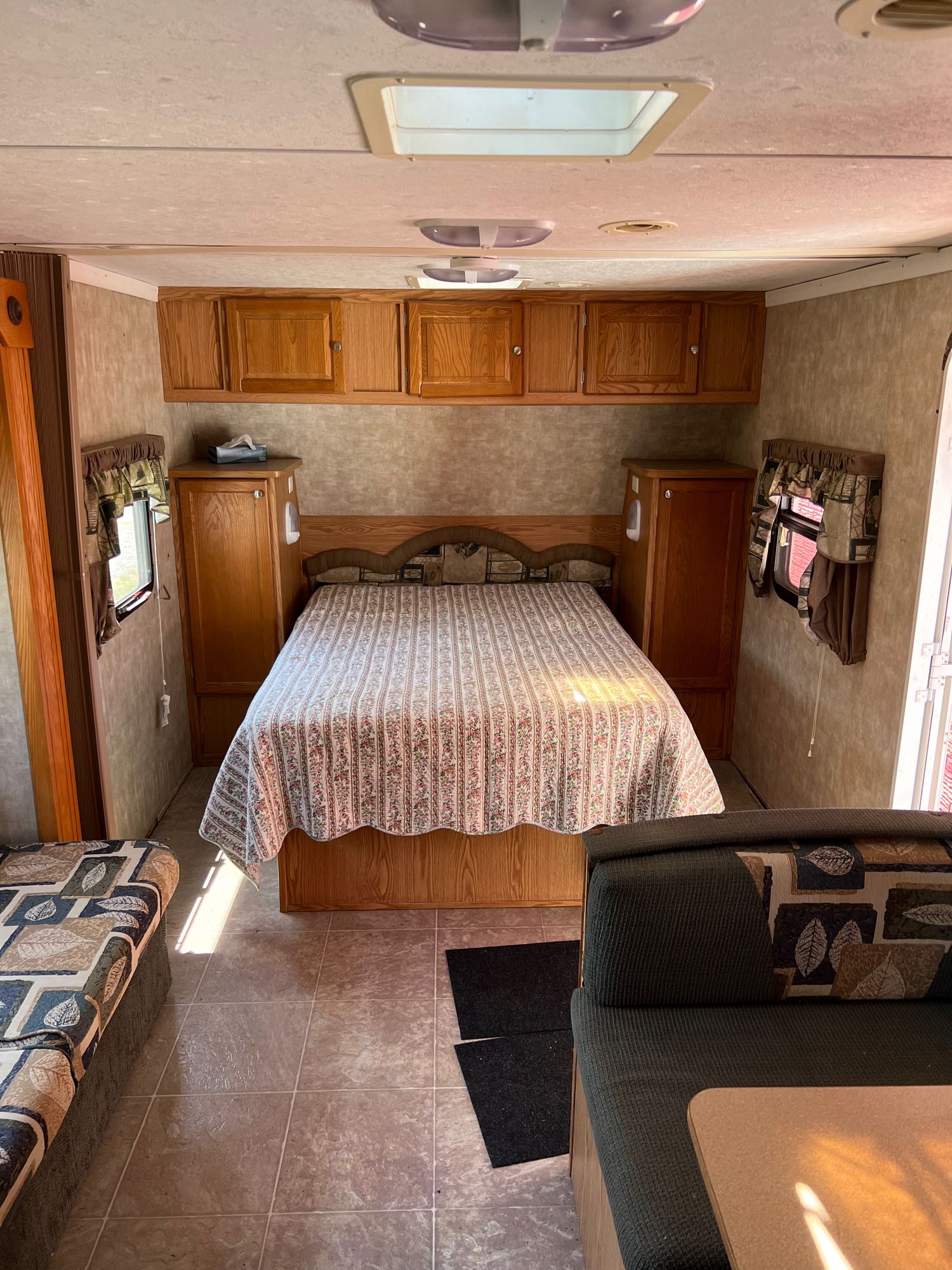 Bright RV rental interior featuring a bedroom with a patterned bed, wood cabinets, and comfortable living area seating.. Pilgrim International Inc Cirrus 24 CRB 2006