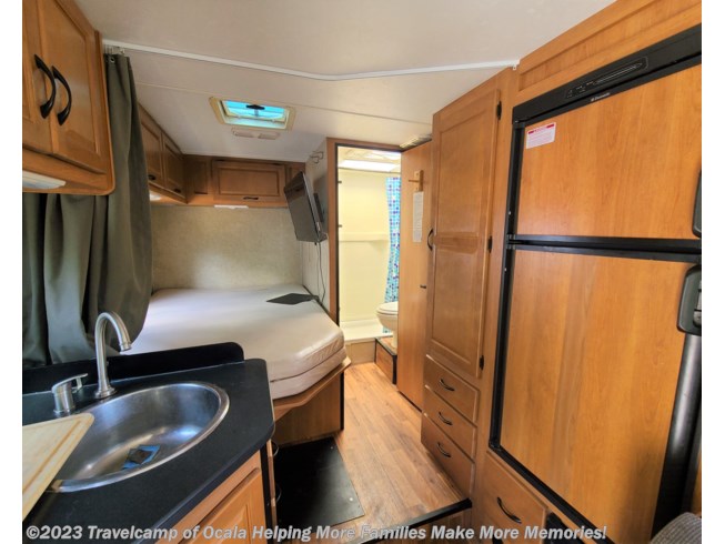 Inside a compact RV rental, showcasing a comfortable bed, functional kitchen with sink, fridge, and bathroom access.. Thor Motor Coach Four Winds Majestic 2015