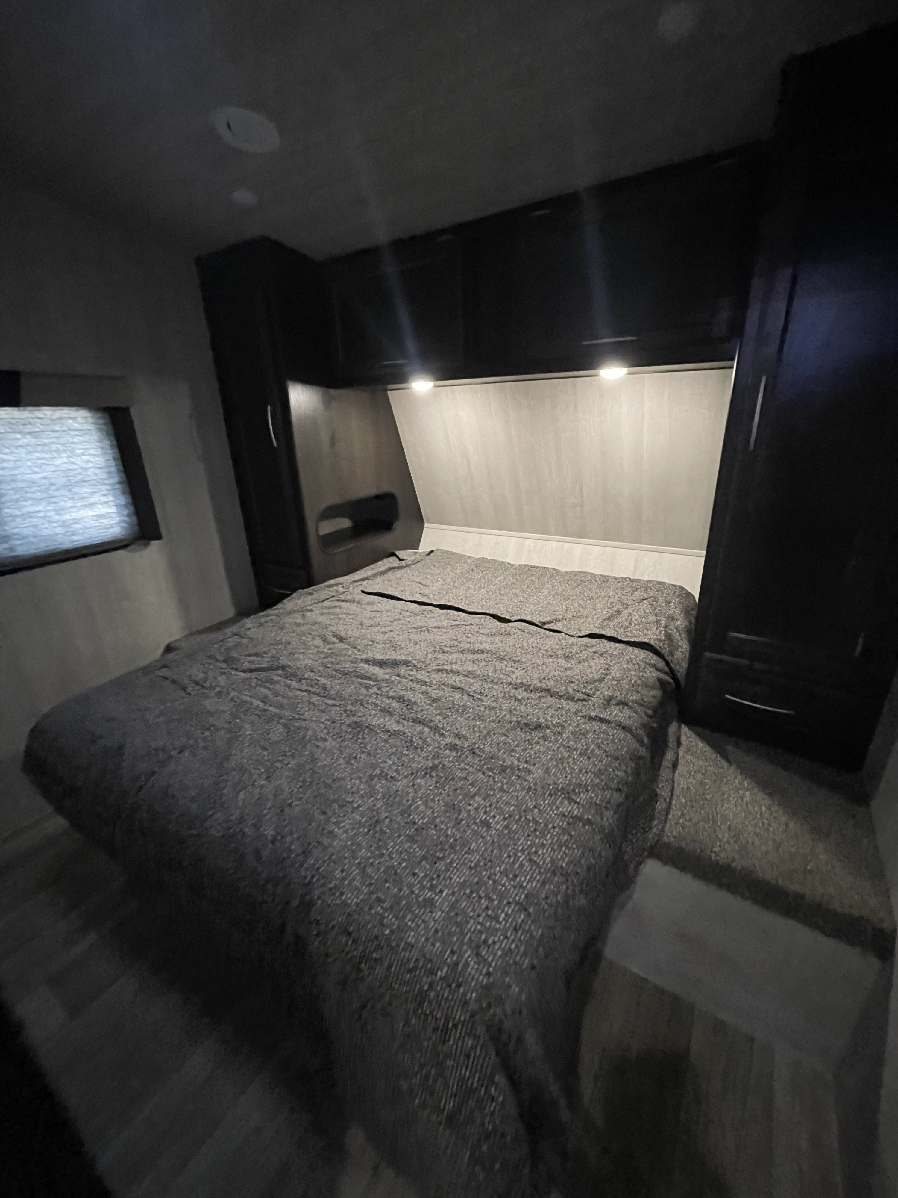 RV rental bedroom: cozy space with a gray bed, overhead storage, and bright reading lights. Ideal for mobile living.. Genesis Supreme Rv Genesis Supreme 2024