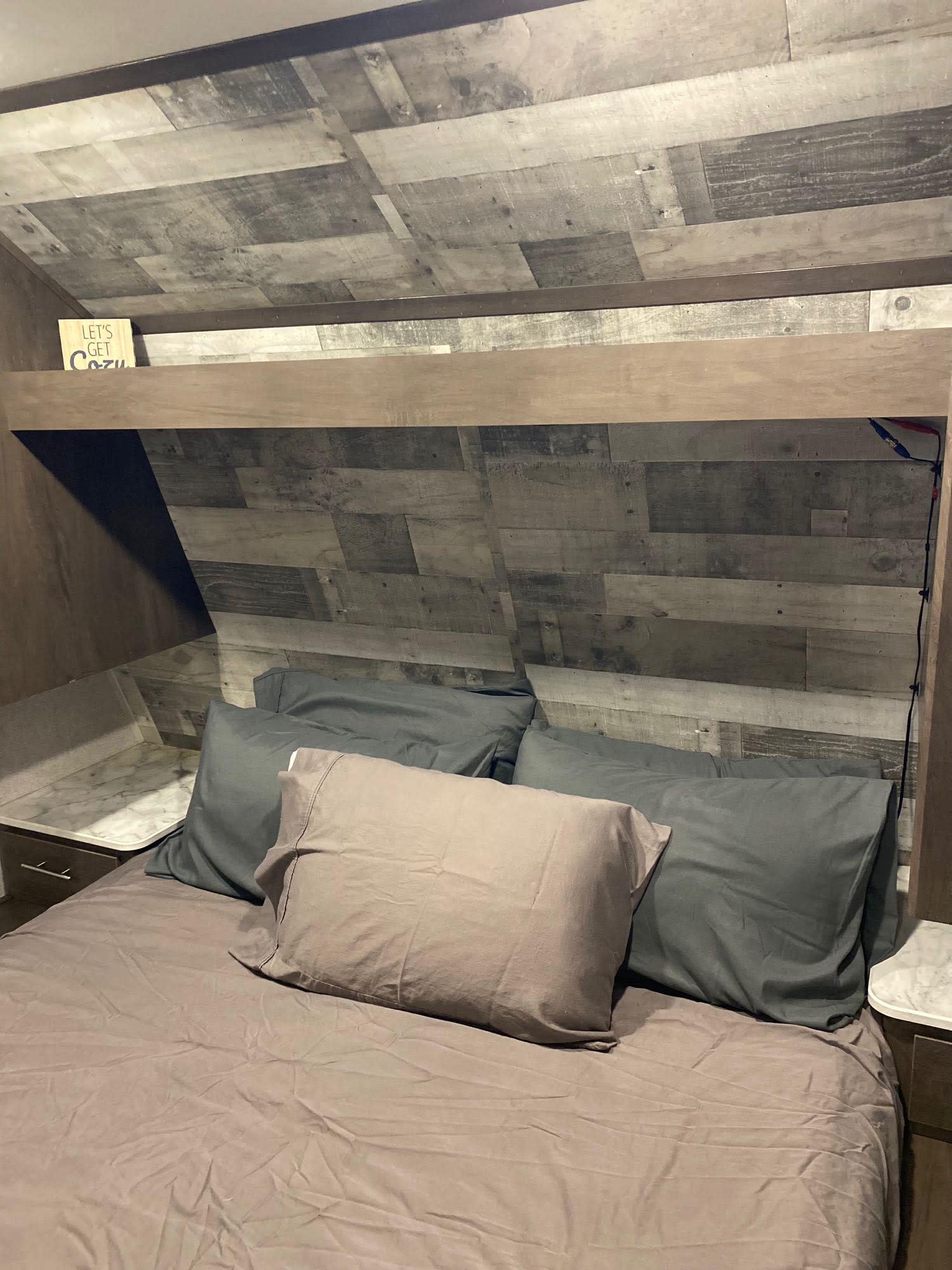 Cozy RV rental bedroom with wood-plank headboard, comfy pillows, and compact side tables. Perfect for travel comfort.. Coleman Lantern 2021