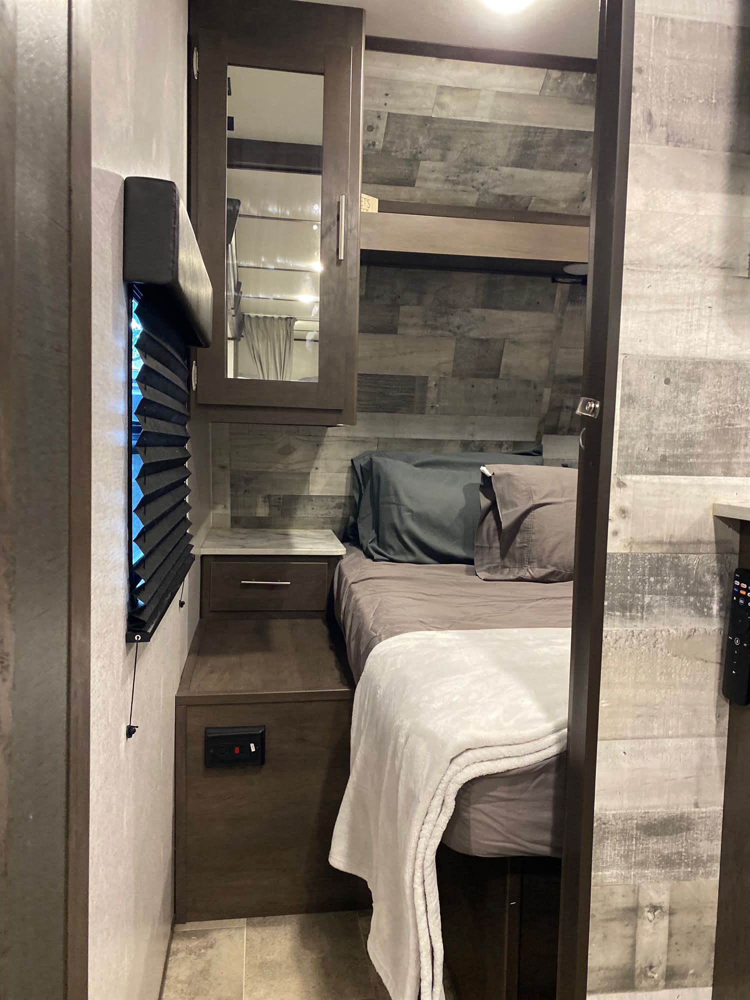 Inside a cozy RV rental bedroom: features a comfortable bed, nightstand, mirrored cabinet, and window blind.. Coleman Lantern 2021
