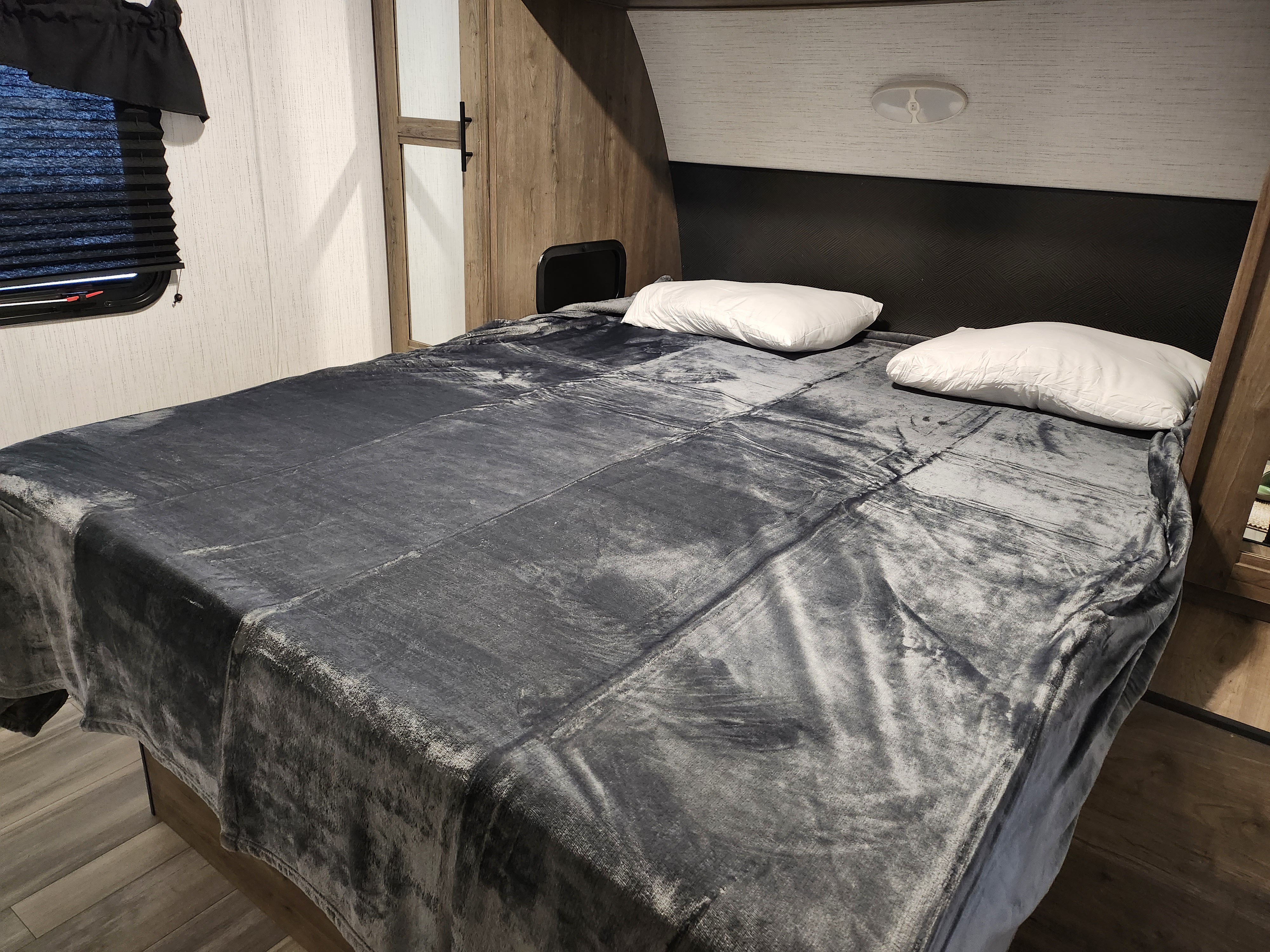 Cozy RV rental bedroom featuring a made bed with a gray blanket, white pillows, and a window.. HEARTLAND PIONEER BH270 2024