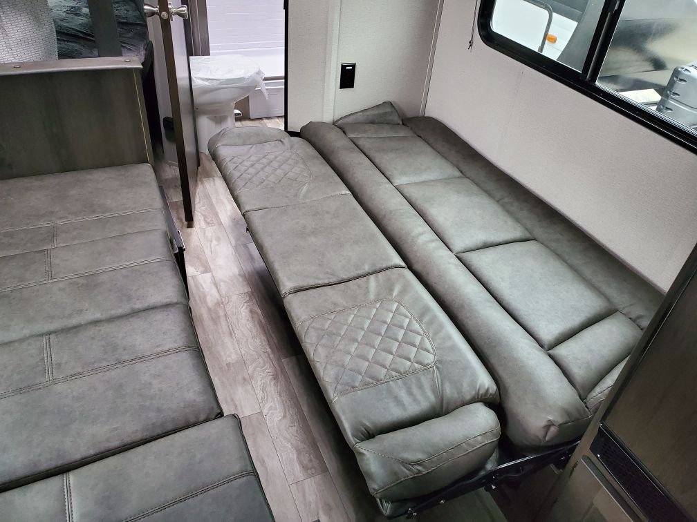 RV rental interior: gray upholstered convertible dinette and a folded-out bed, with an adjacent bathroom.. Grand Design Transcend Xplor 2021