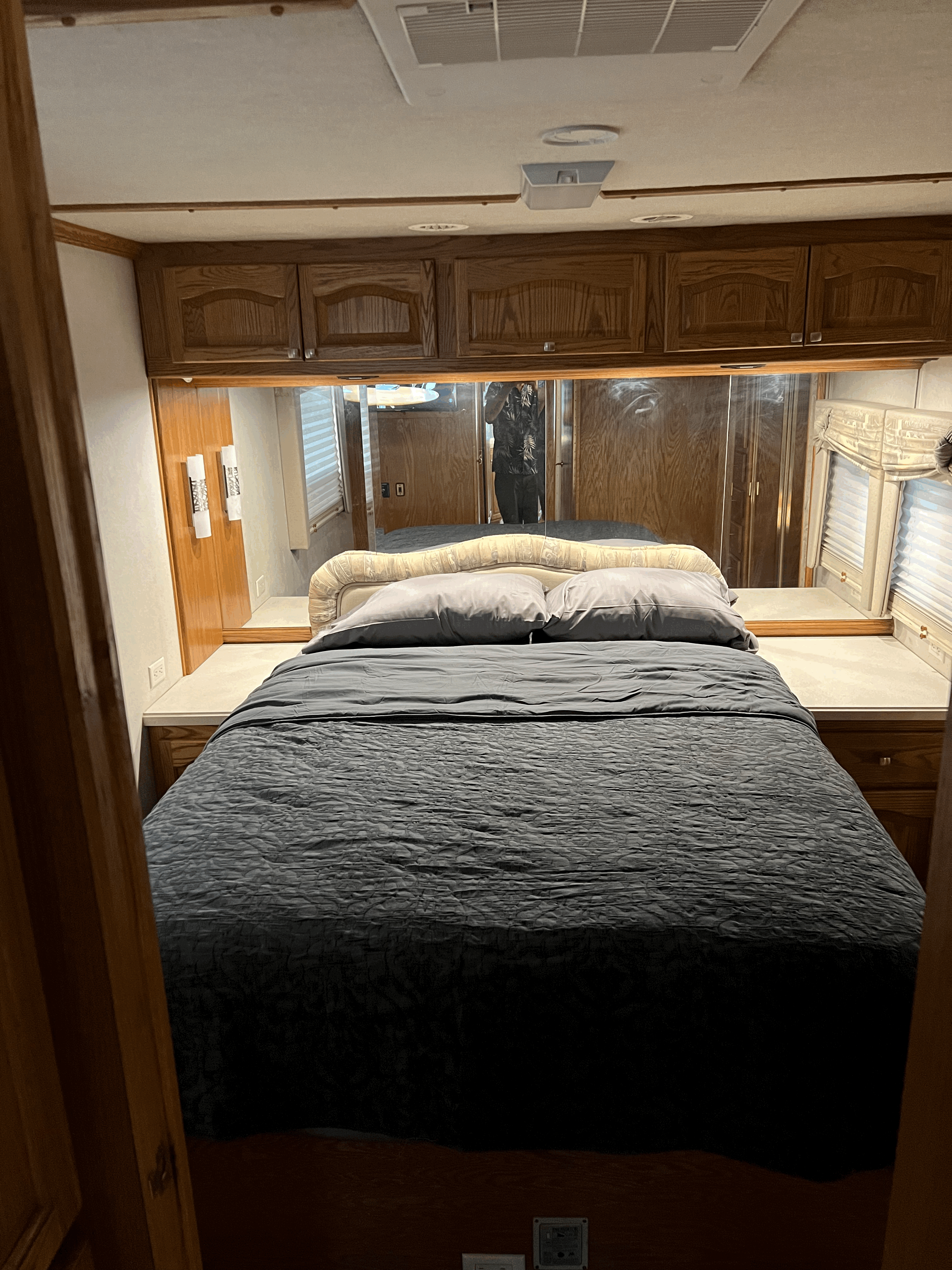 Cozy RV rental bedroom features a neatly made bed with grey bedding, overhead wooden cabinets, and mirrored walls.. Allegro Allegro Bus 2001