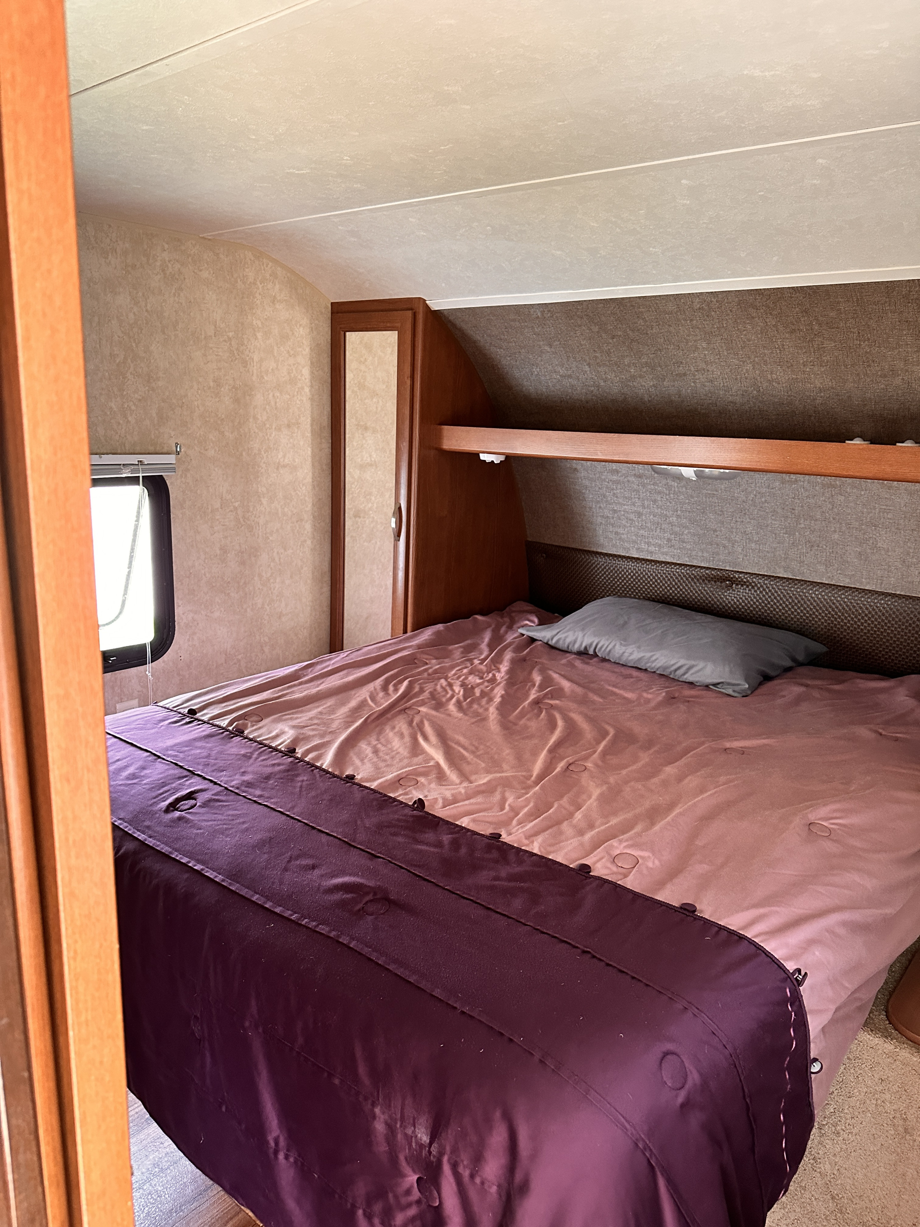 Cozy RV rental bedroom with a bed featuring pink & purple bedding, built-in storage, and a window.. Forest River Salem 2016