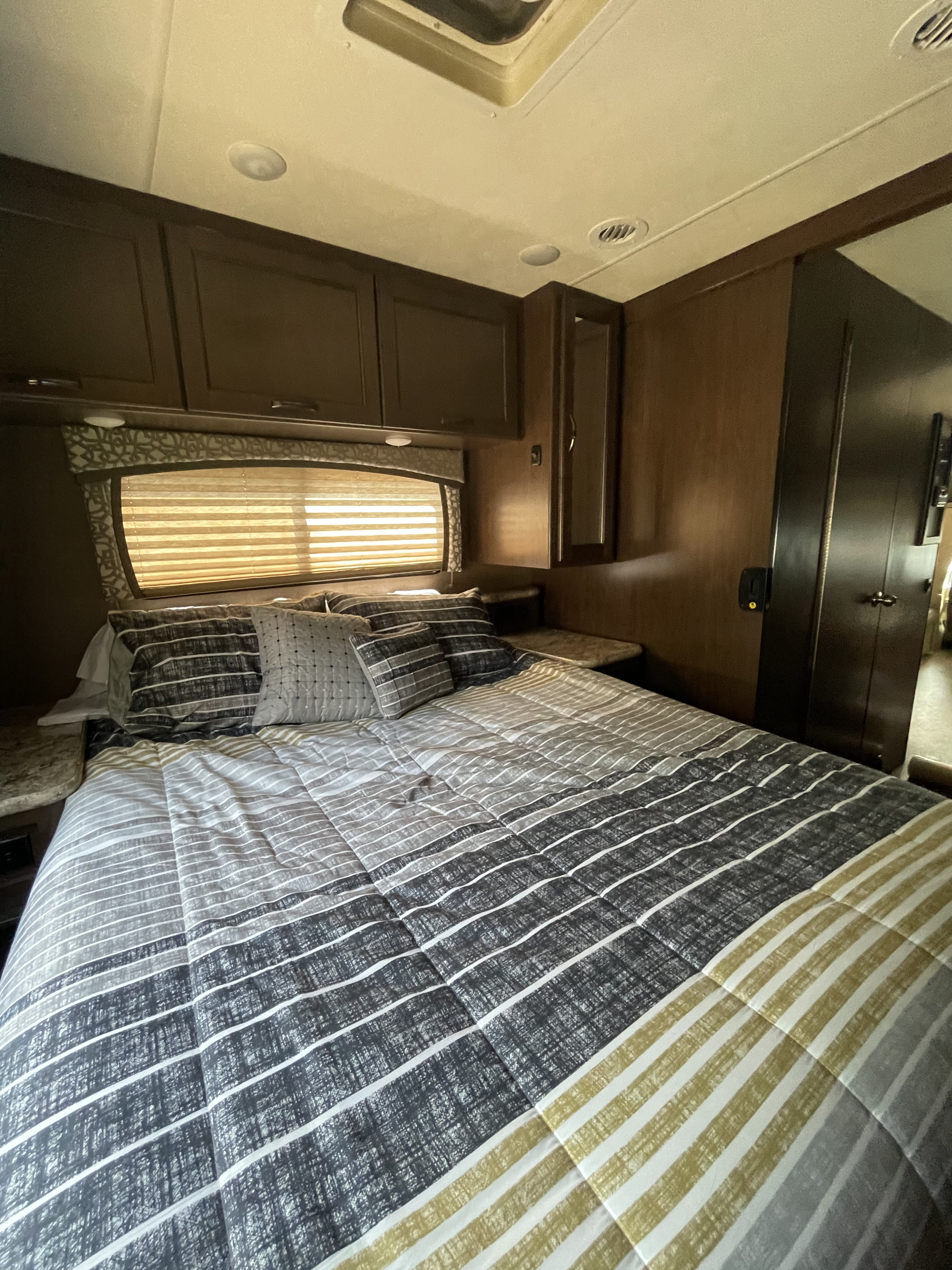RV rental bedroom with stylish striped bedding, built-in storage, and window for natural light.. Thor Chateau 2019