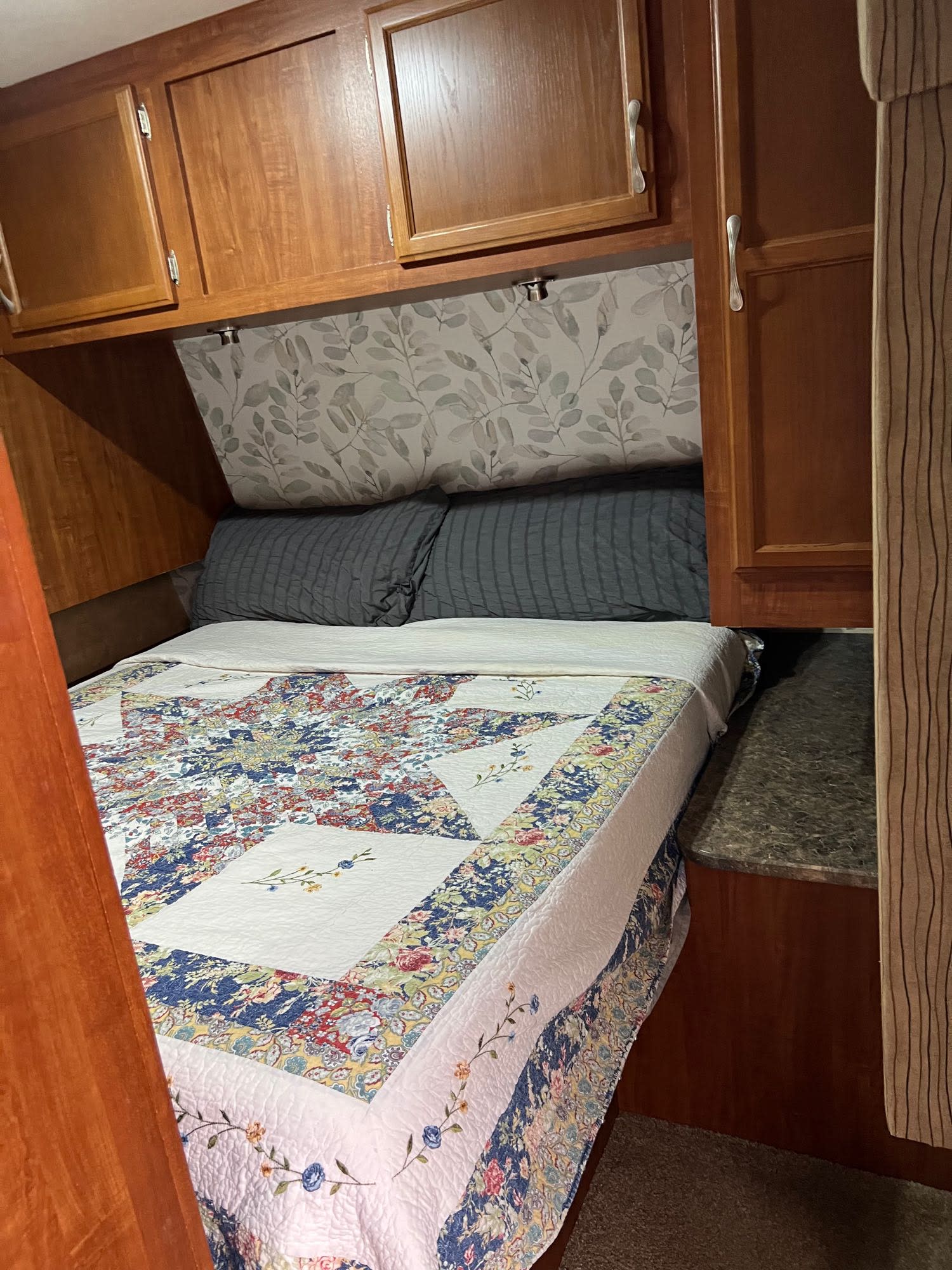 Cozy RV rental bedroom featuring a colorful quilt on the bed, grey pillows, and wooden overhead storage cabinets.. Jayco Camper Trailer- Eagle 2011