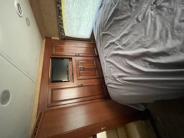 RV rental bedroom interior featuring a cozy bed, integrated TV, and rich wood cabinetry.. Forest River Forester 317DS 2014