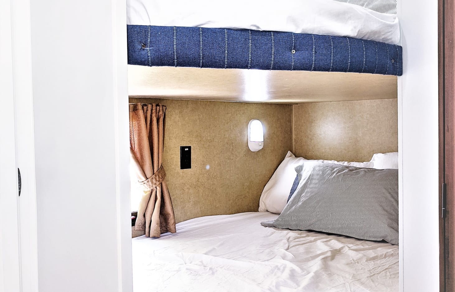 Cozy bunk beds in an RV rental. White bedding, striped pillow, window with brown curtains, and a wall light in compact interior.. Jayco Jay Flight Swift 2014