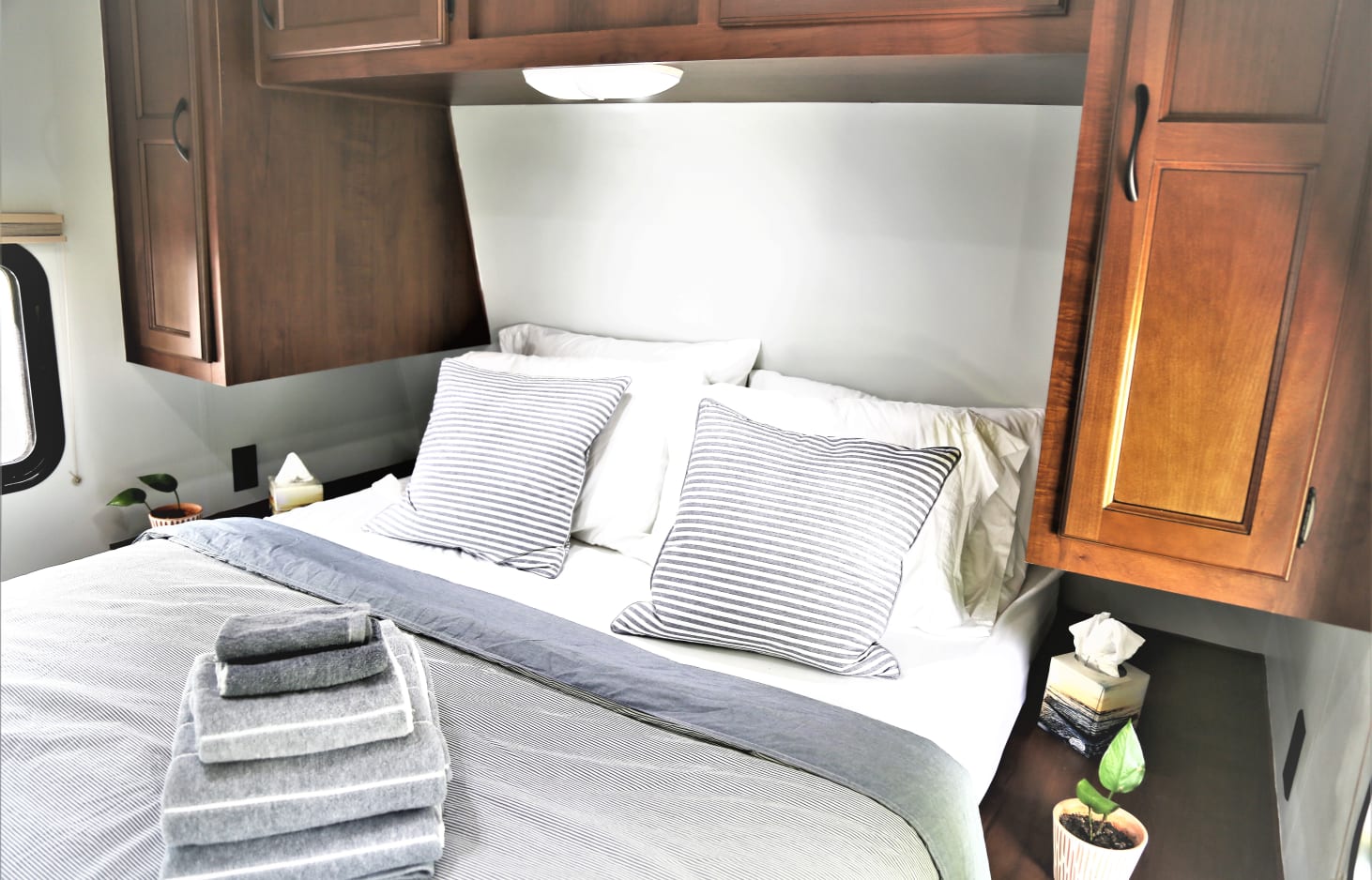 Cozy RV rental bedroom with a bed, striped pillows, folded towels, and wooden overhead cabinets. Enjoy your trip!. Jayco Jay Flight Swift 2014