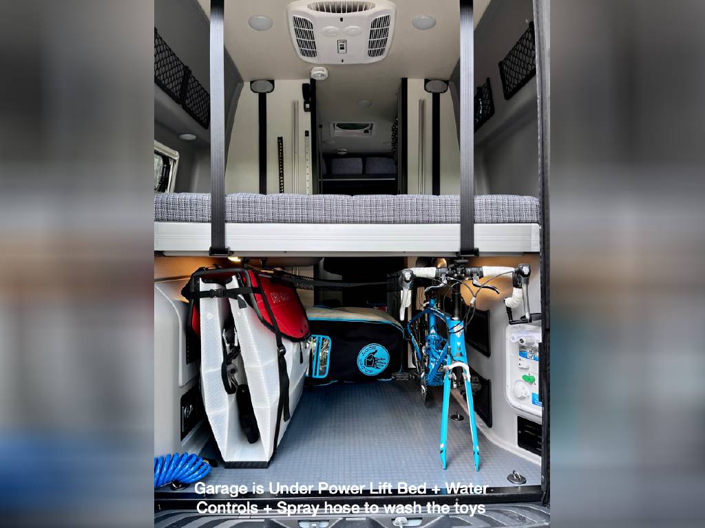 RV rental: Camper van interior with power lift bed over gear garage, storing a bike, paddleboard, and wash hose.. Winnebago Revel 2022