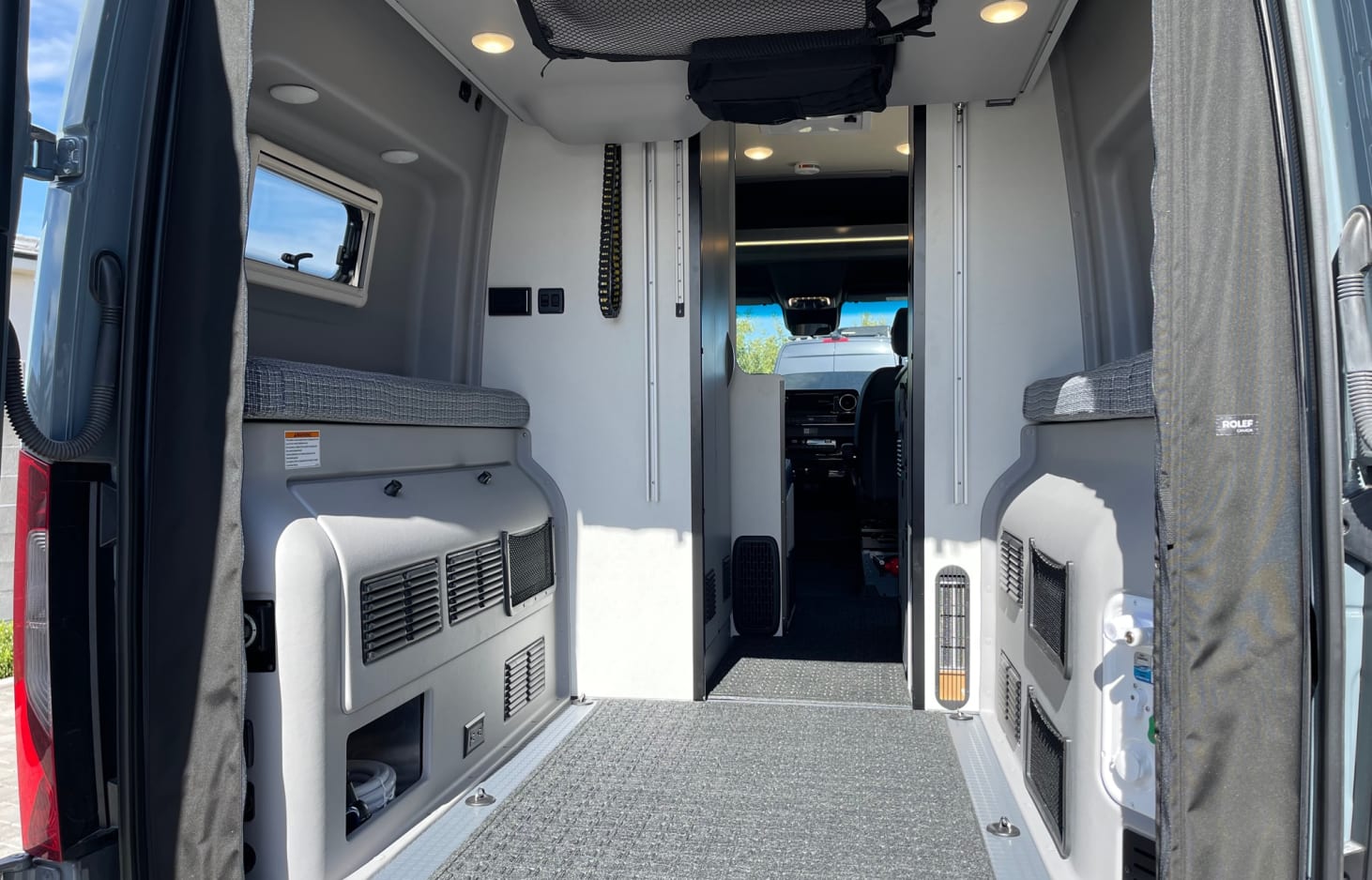 Spacious RV rental interior: rear view of bench beds, storage panels, mesh net, and front cockpit.. Winnebago Revel 2022